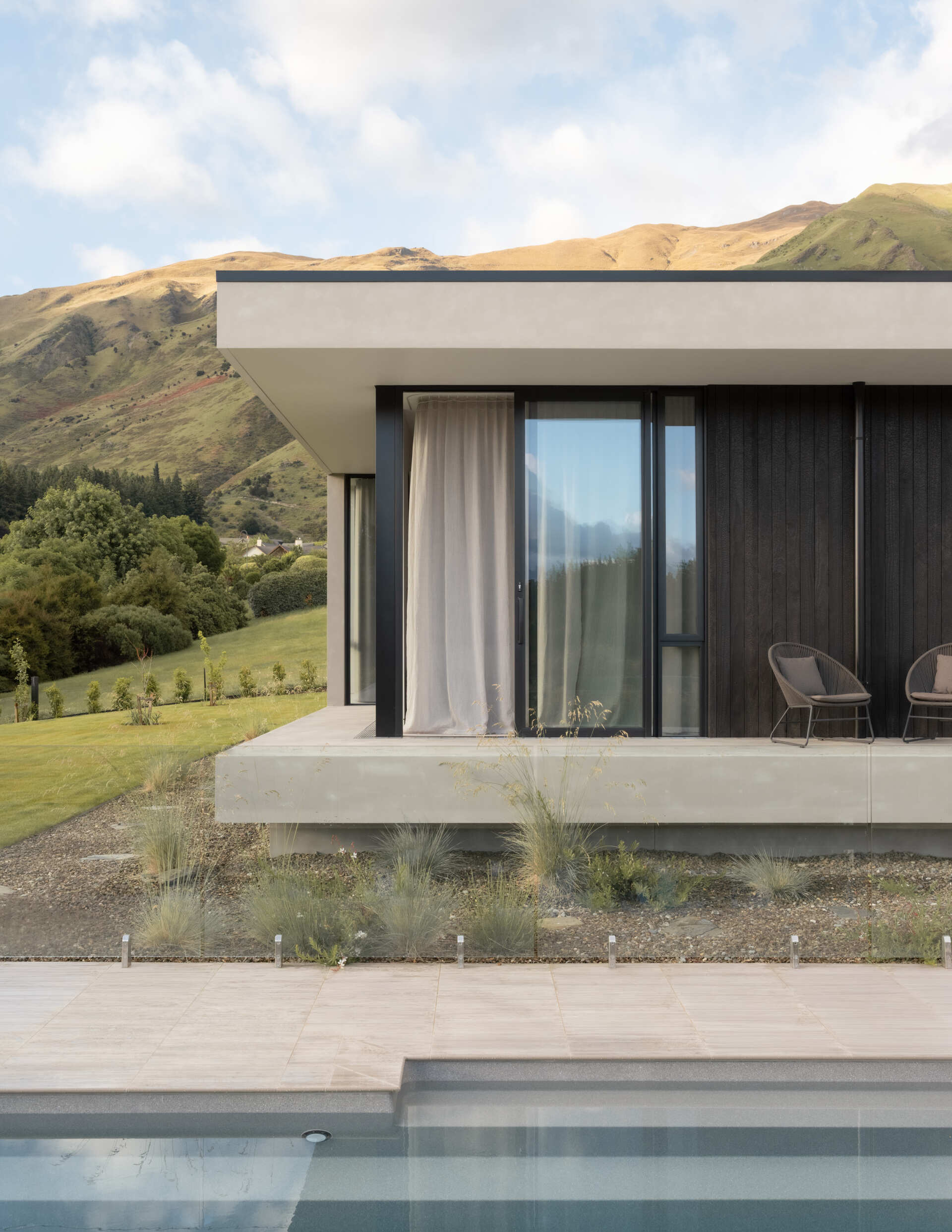 Explore a contemporary hillside house in W?naka featuring stepped architecture, floating concrete terraces, floor-to-ceiling windows, mountain views, and landscaped gardens with sculptural artworks.