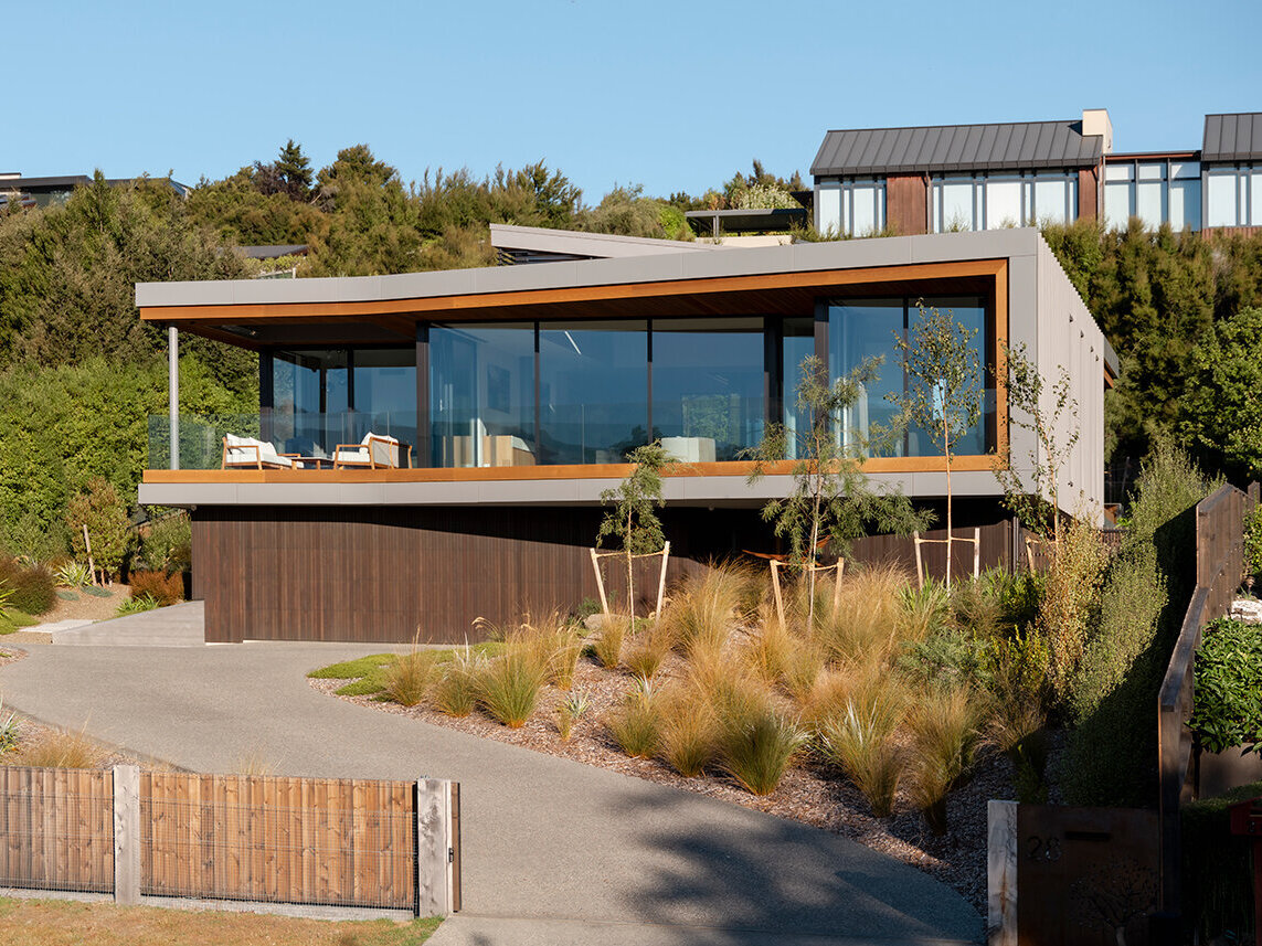 Contemporary New Zealand house by Condon Scott Architects featuring an angled metal roof, expansive glass walls, warm wood accents, and a floating upper floor above dark-stained cedar cladding.