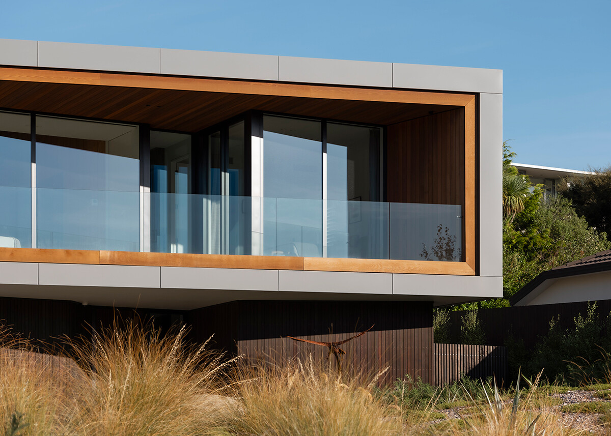 Close-up of a contemporary house balcony featuring a light metal frame, warm wood ceiling and walls, floor-to-ceiling glass doors, and a transparent glass railing.