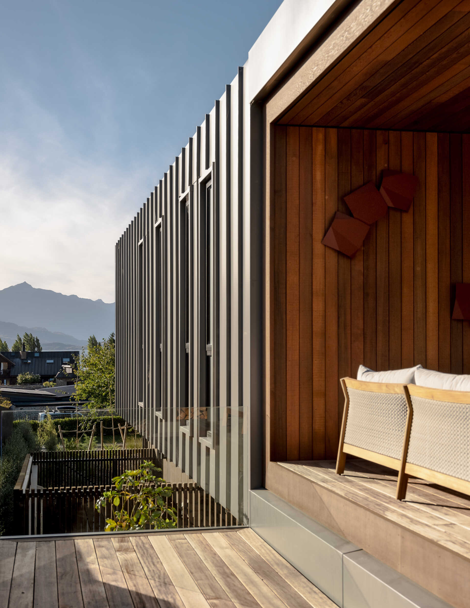 Contemporary house exterior featuring light-colored vertical metal cladding and a recessed wood-lined balcony. A narrow window, glass railing, and outdoor sofa add detail to the sheltered upper-floor space.