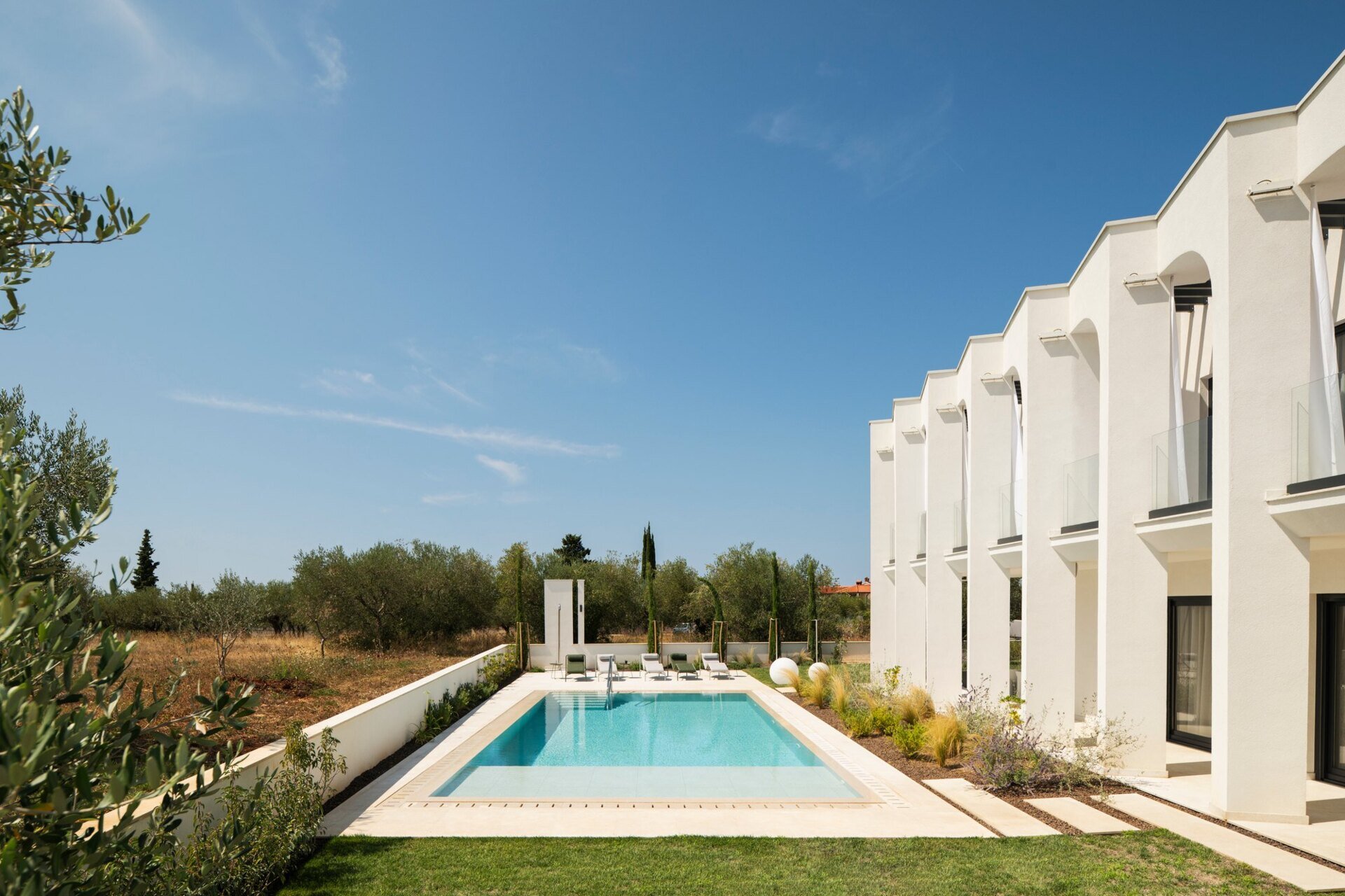 Explore the swimming pool and south-facing façade of Arc House, a modern villa in Istria, Croatia. A rectangular pool, sculptural concrete arches, covered balconies and Mediterranean landscaping create an impressive contemporary outdoor living area.