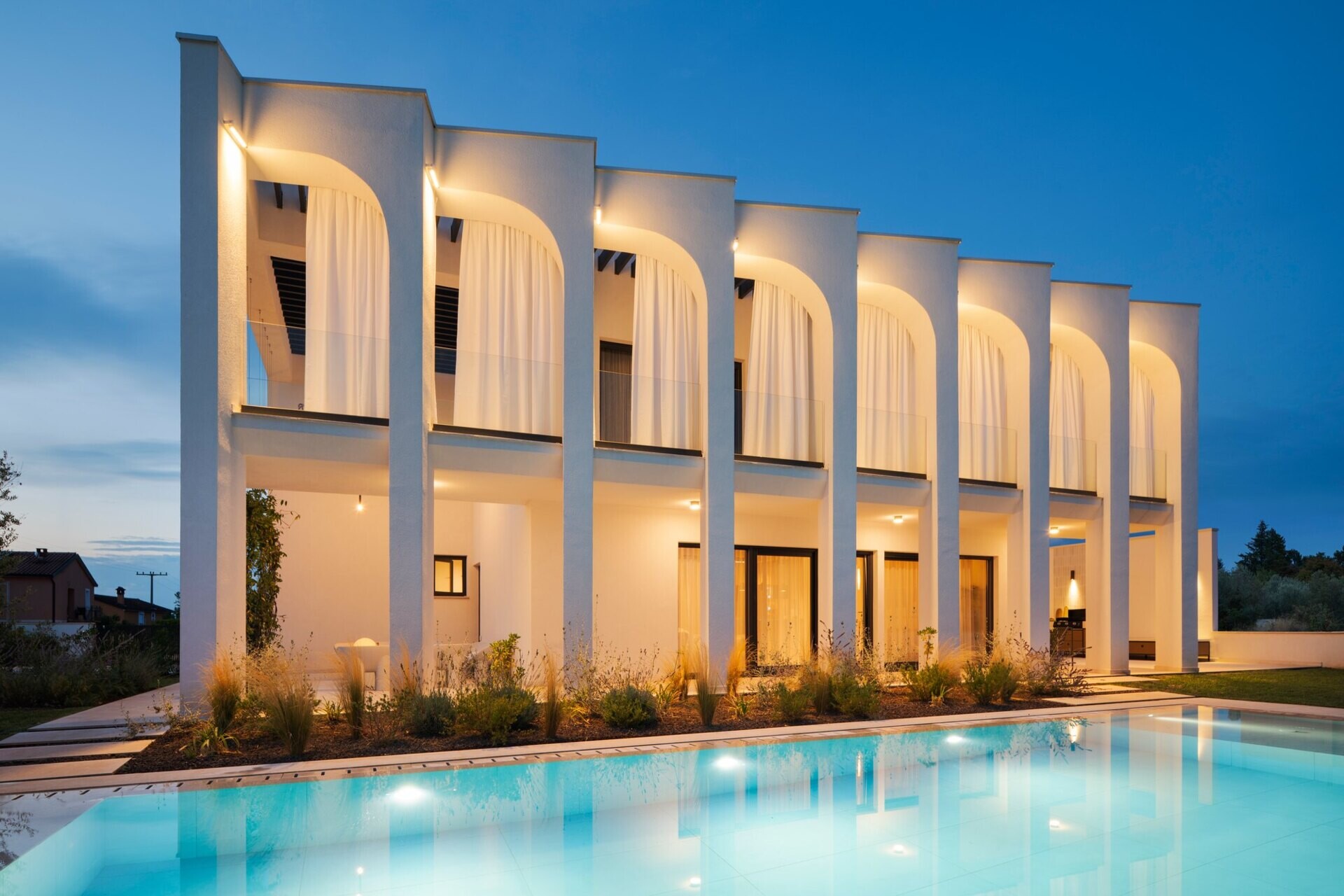Explore the swimming pool and south-facing façade of Arc House, a modern villa in Istria, Croatia. A rectangular pool, sculptural concrete arches, covered balconies and Mediterranean landscaping create an impressive contemporary outdoor living area.