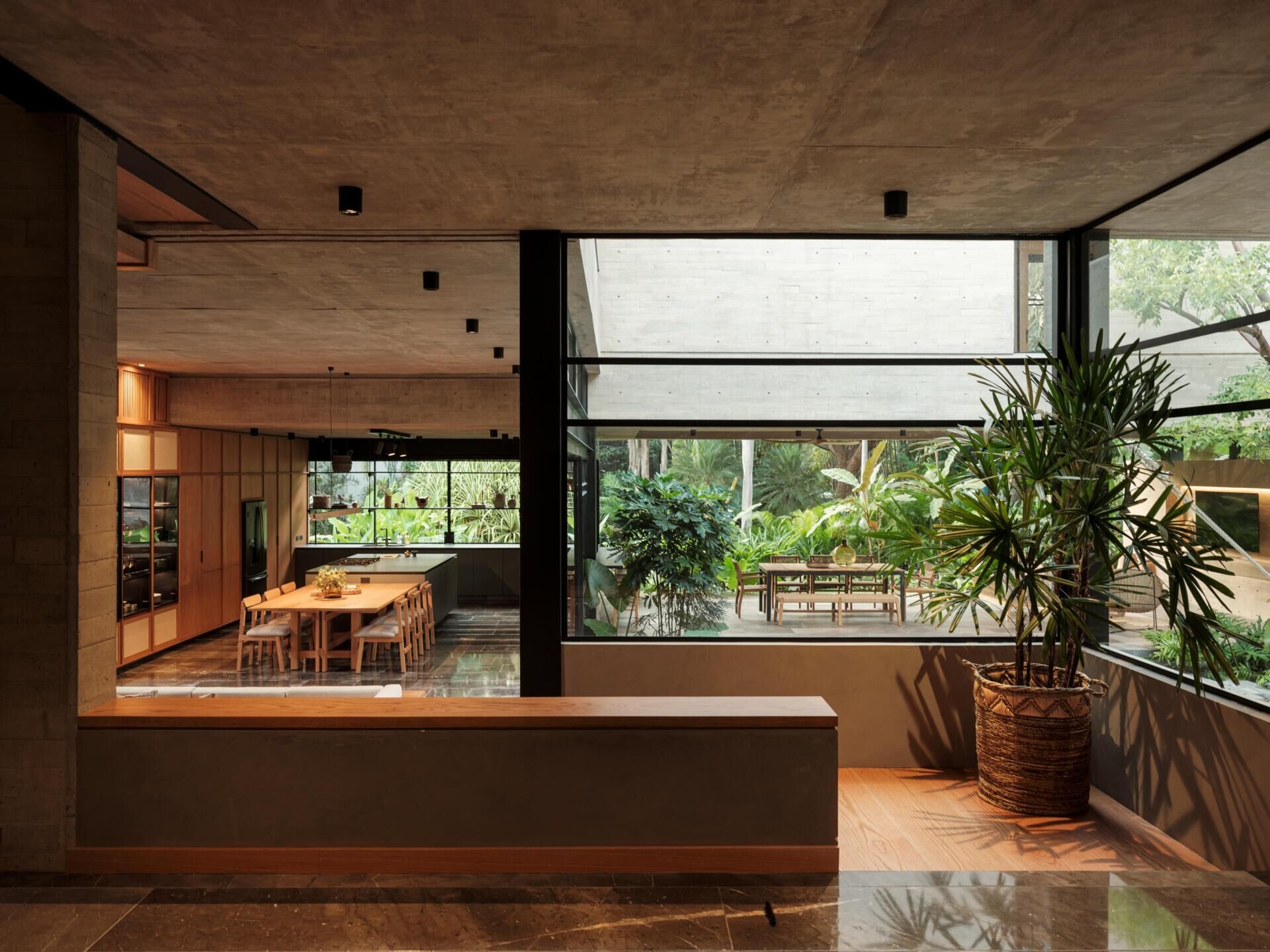 Step inside Casa Akina by Di Frenna arquitectos in Mexico, where a modern entryway features concrete ceilings, dark stone floors, steel-framed windows, warm wood details, and views of a lush garden.