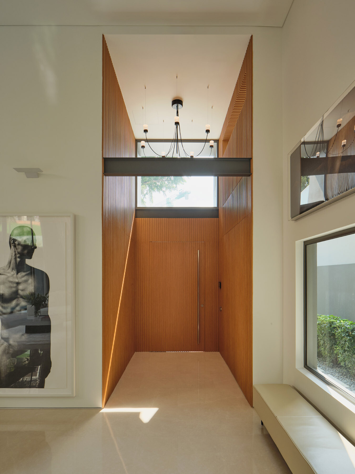 Step inside the entrance of JS-House, where a timber-lined porch leads to a double-height foyer with vertical wood panelling, sculptural lighting, and natural light.