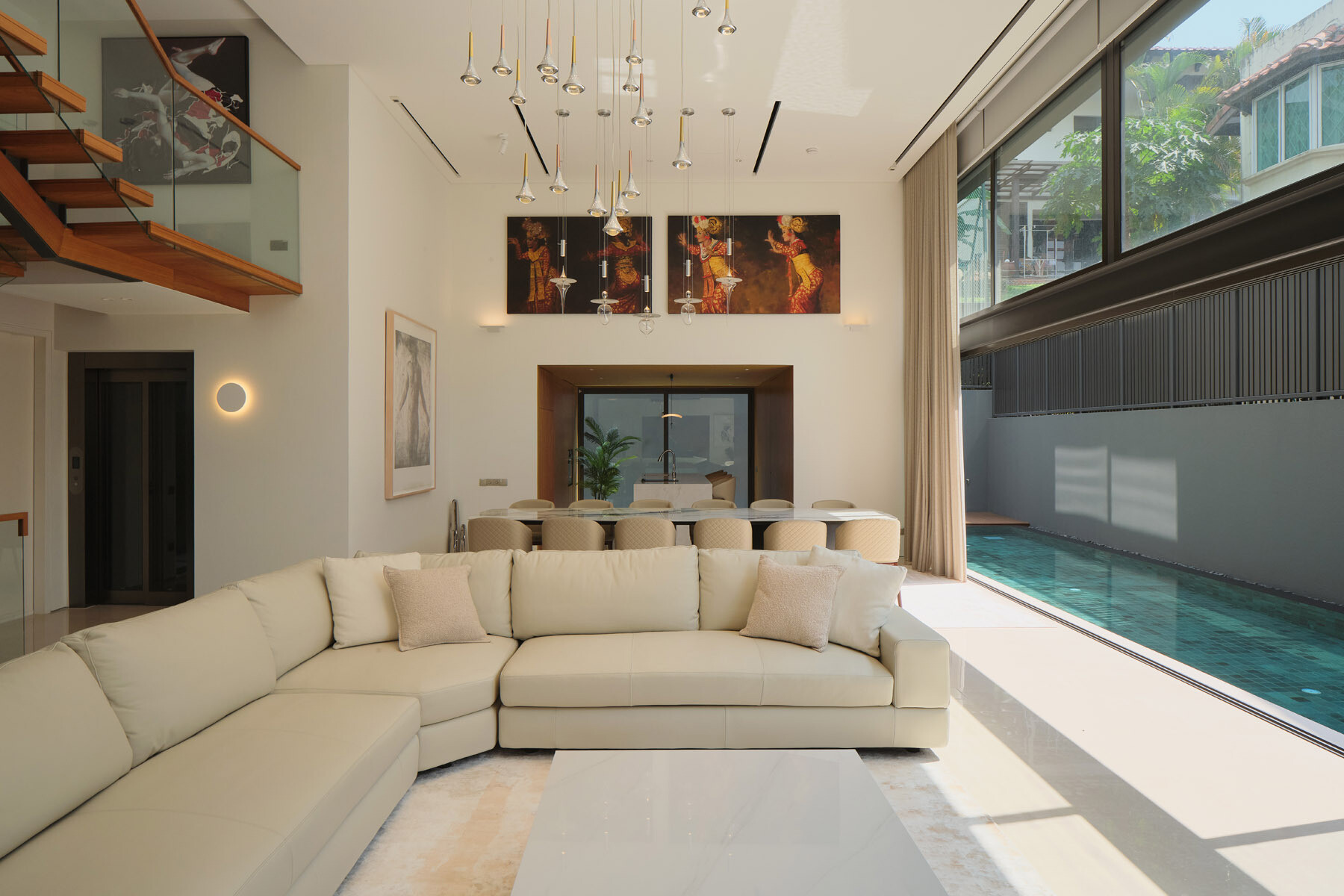 Explore the bright living room of JS-House, featuring a cream sectional sofa, contemporary pendant lighting, polished stone floors, and large sliding doors overlooking the swimming pool.