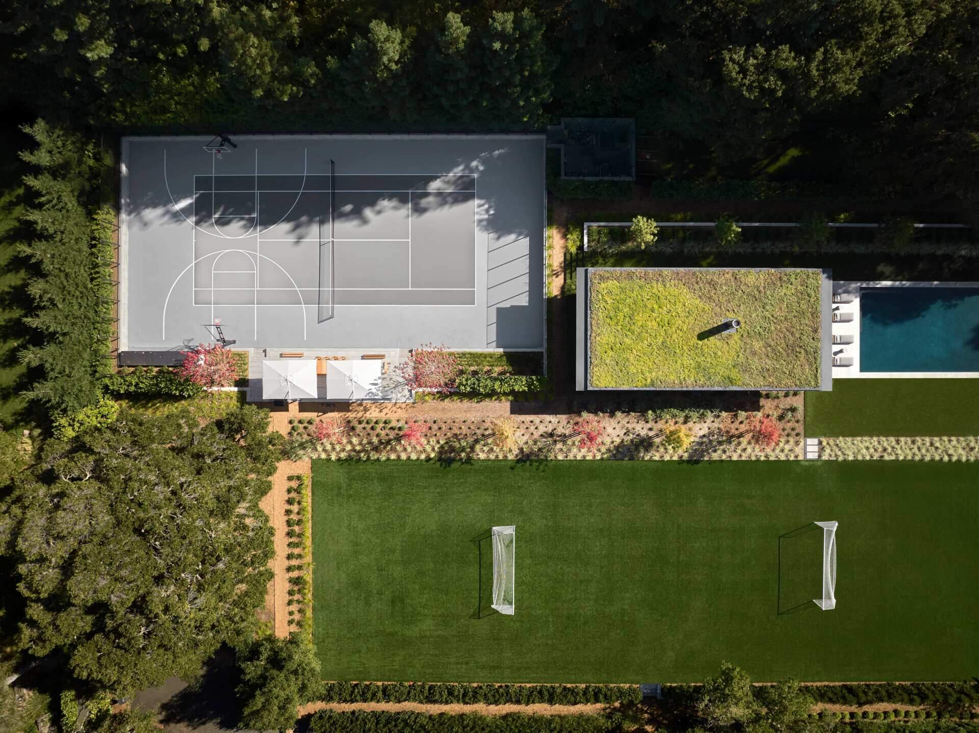 Explore the recreational facilities at this 3.5-acre California home, featuring a private tennis and basketball court, soccer field, and outdoor entertaining terrace. Timber furniture, white umbrellas, and landscaped gardens create a welcoming space for sports and social gatherings.