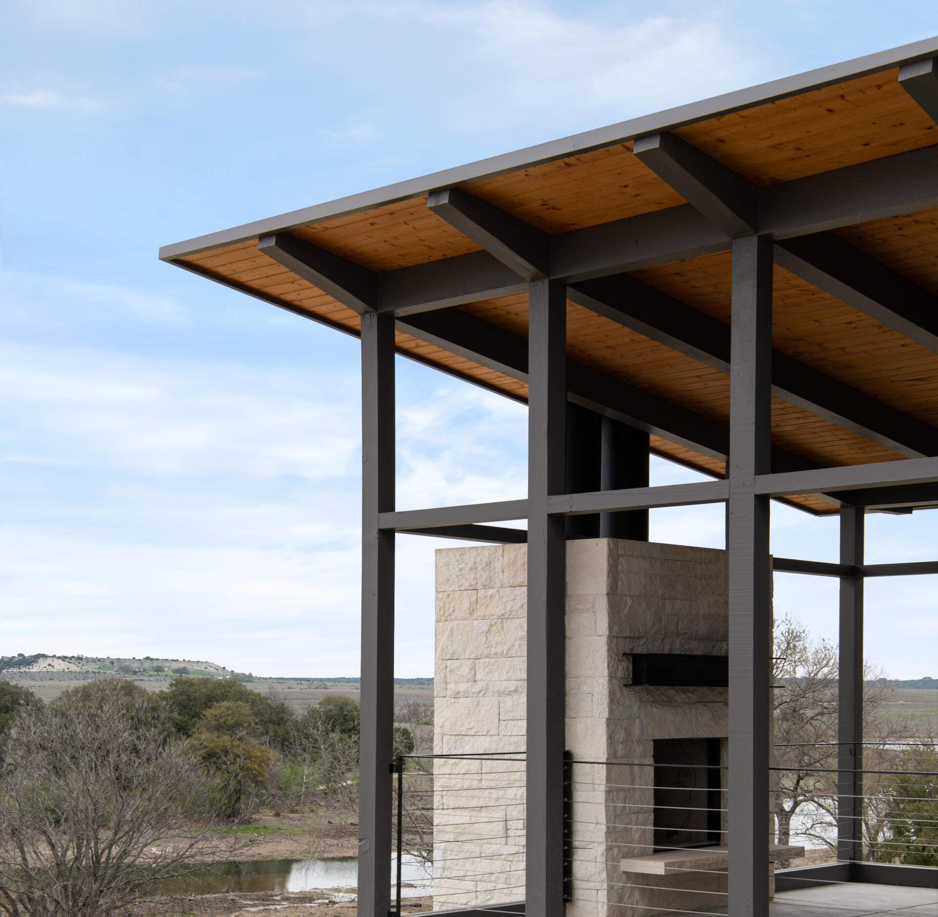 A covered outdoor sitting area features a limestone fireplace, exposed ceiling structure, and views of the Texas landscape.