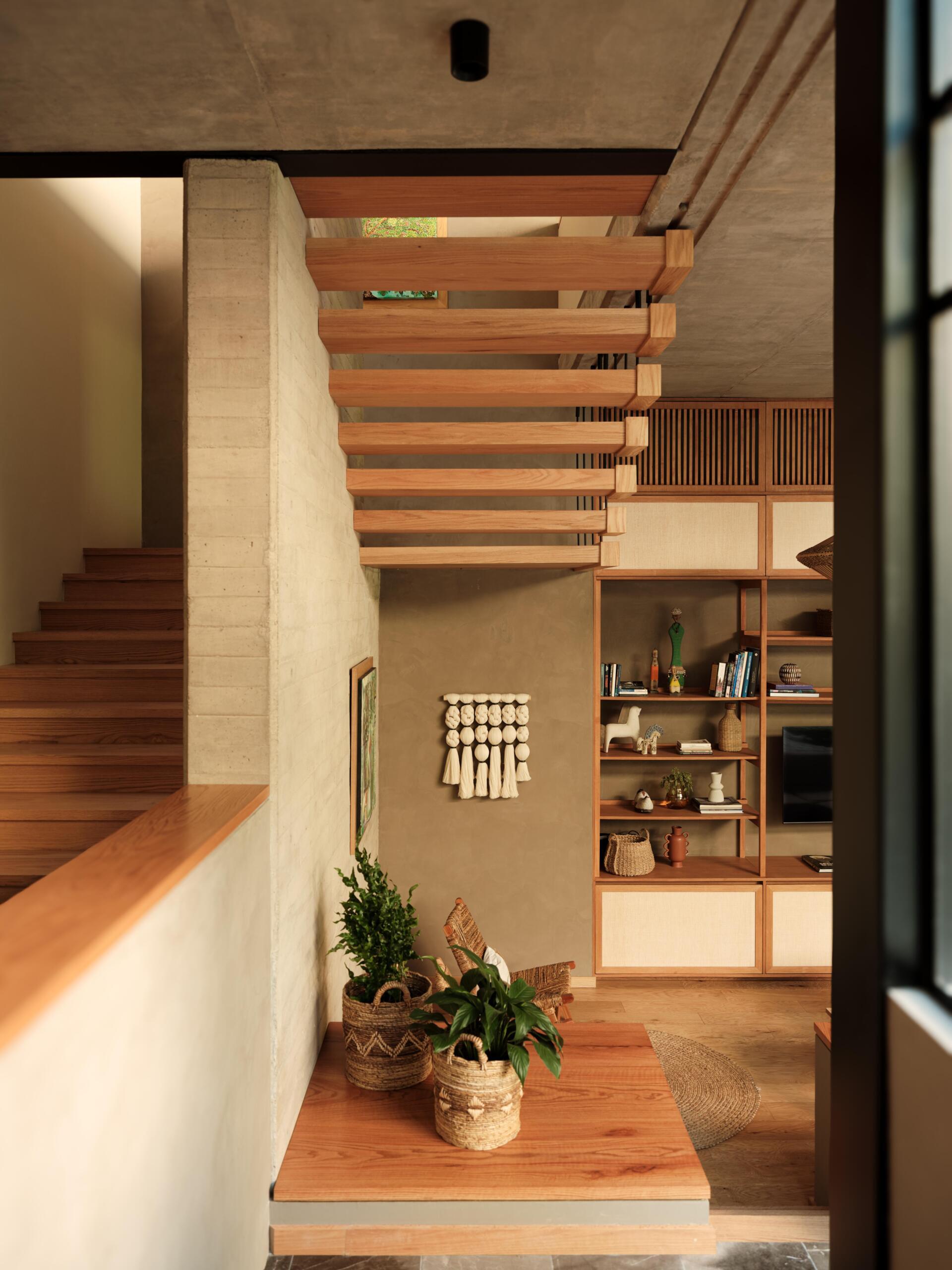 A modern wooden staircase features floating timber treads, slim black metal balusters, and exposed concrete walls. Explore this beautiful staircase design in a contemporary Mexican home.