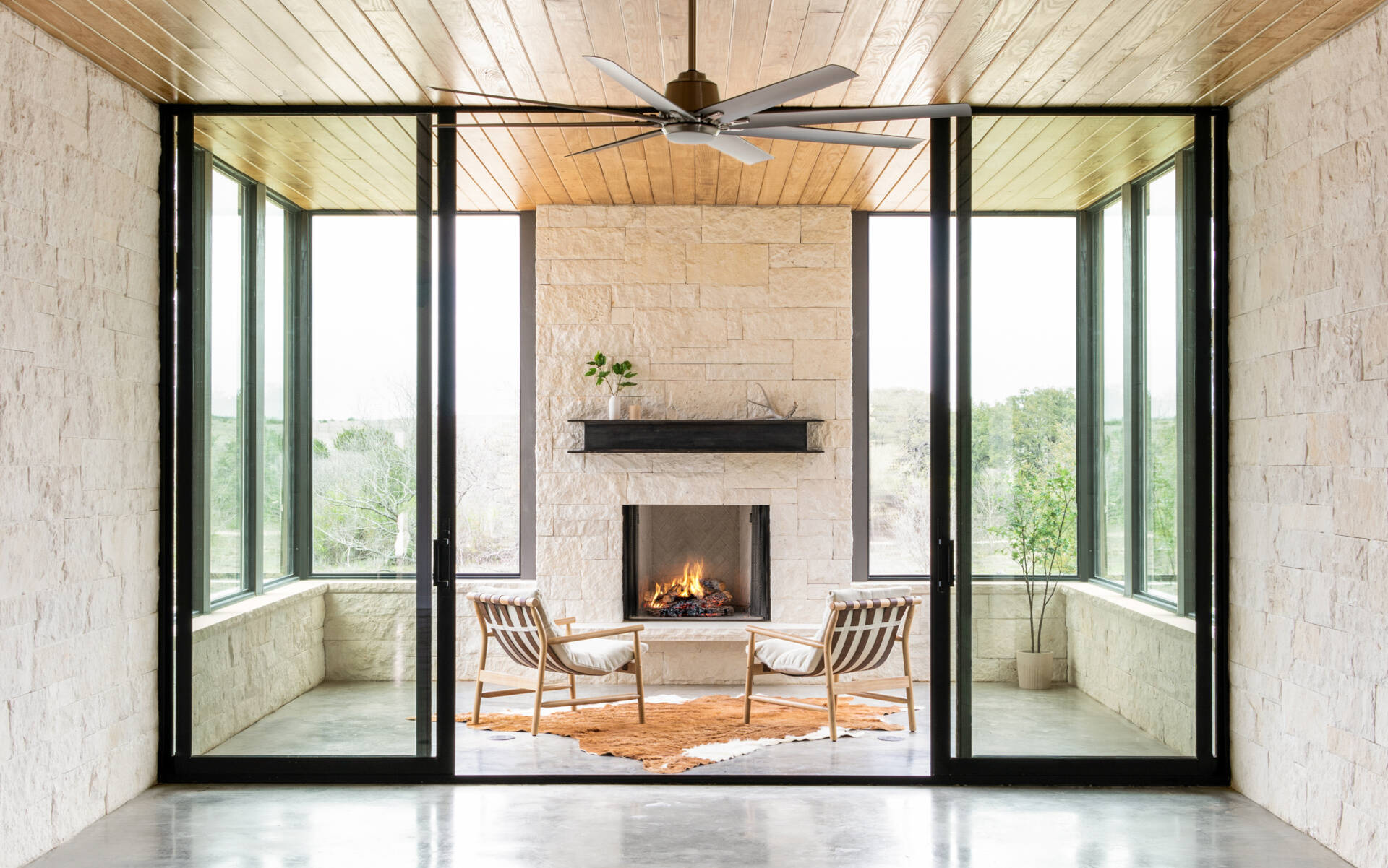 A covered outdoor sitting area features a limestone fireplace, exposed ceiling structure, and views of the Texas landscape.