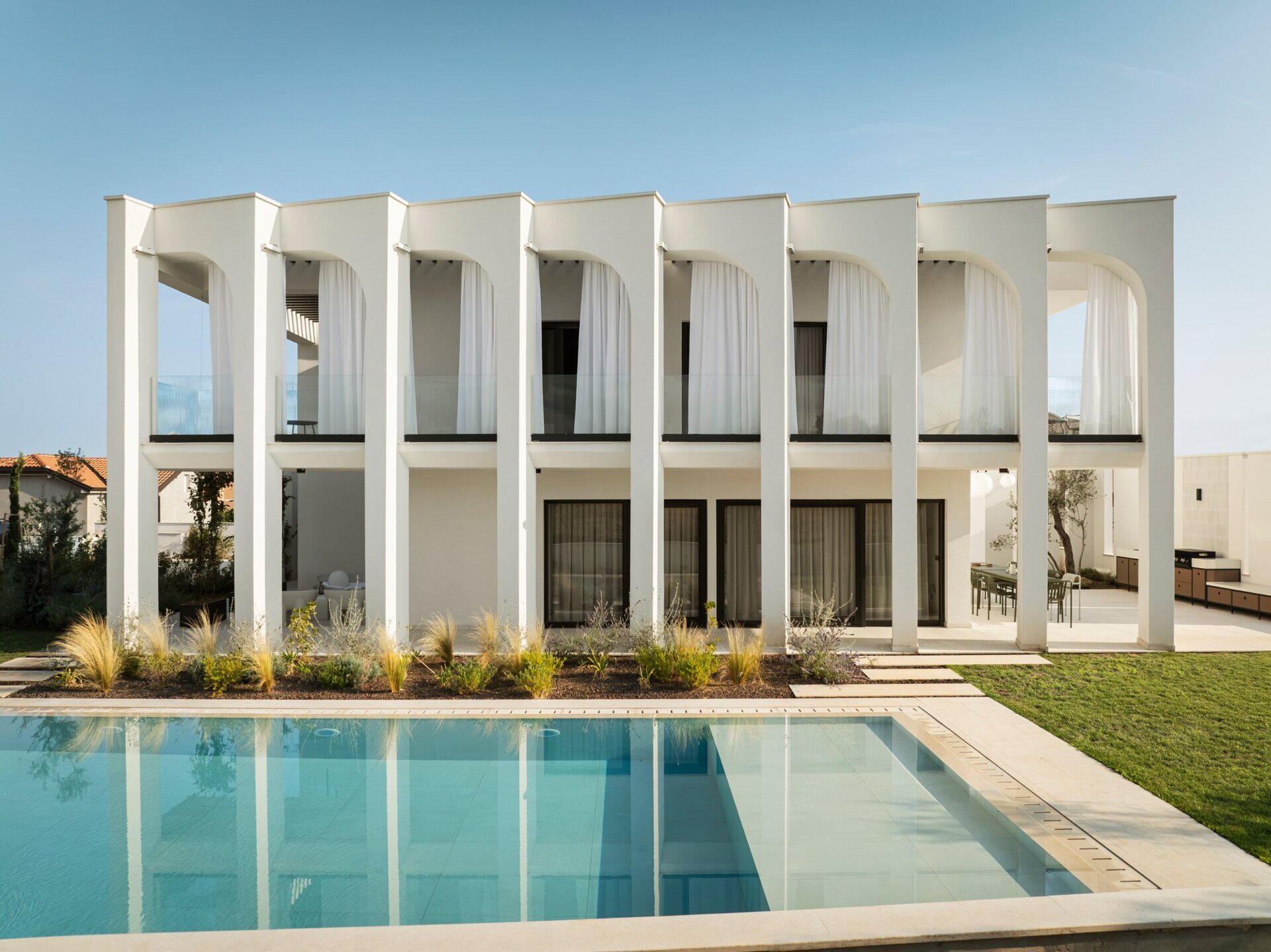 Explore the swimming pool and south-facing façade of Arc House, a modern villa in Istria, Croatia. A rectangular pool, sculptural concrete arches, covered balconies and Mediterranean landscaping create an impressive contemporary outdoor living area.