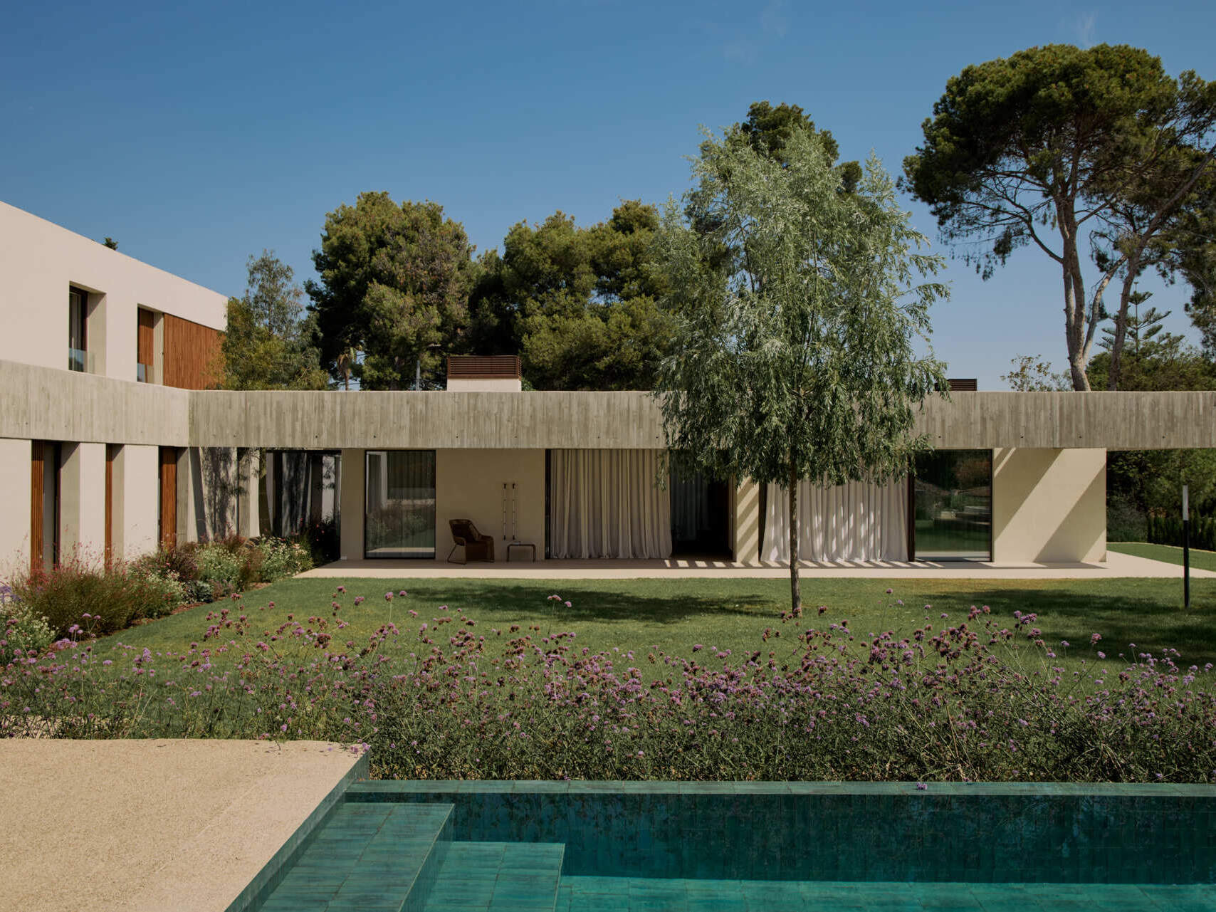 This modern concrete home by Viruta Lab in Valencia, Spain, features an L-shaped floor plan, board-marked concrete walls, horizontal architecture, and landscaped gardens.