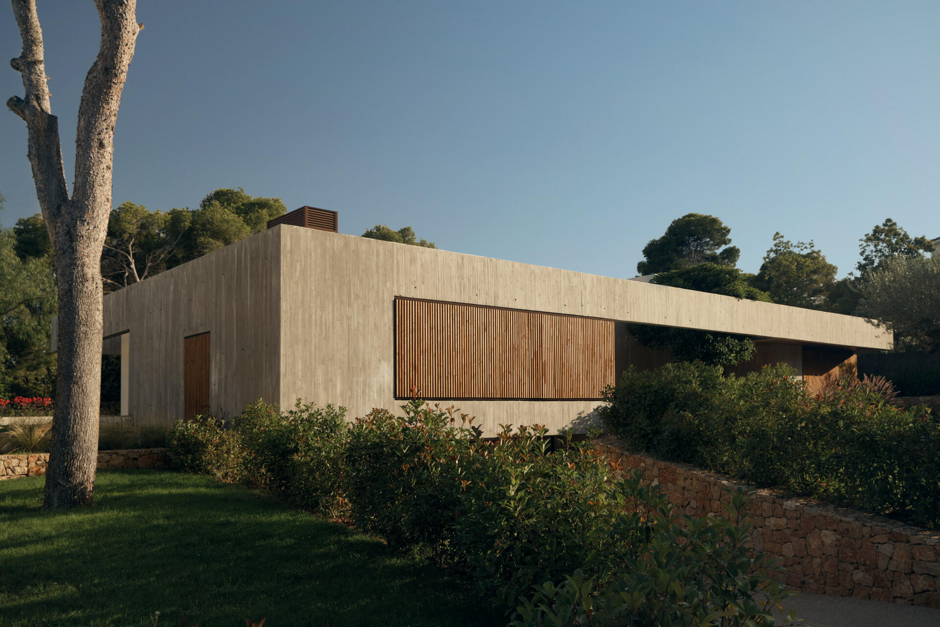 This modern concrete home by Viruta Lab in Valencia, Spain, features an L-shaped floor plan, board-marked concrete walls, horizontal architecture, and landscaped gardens.