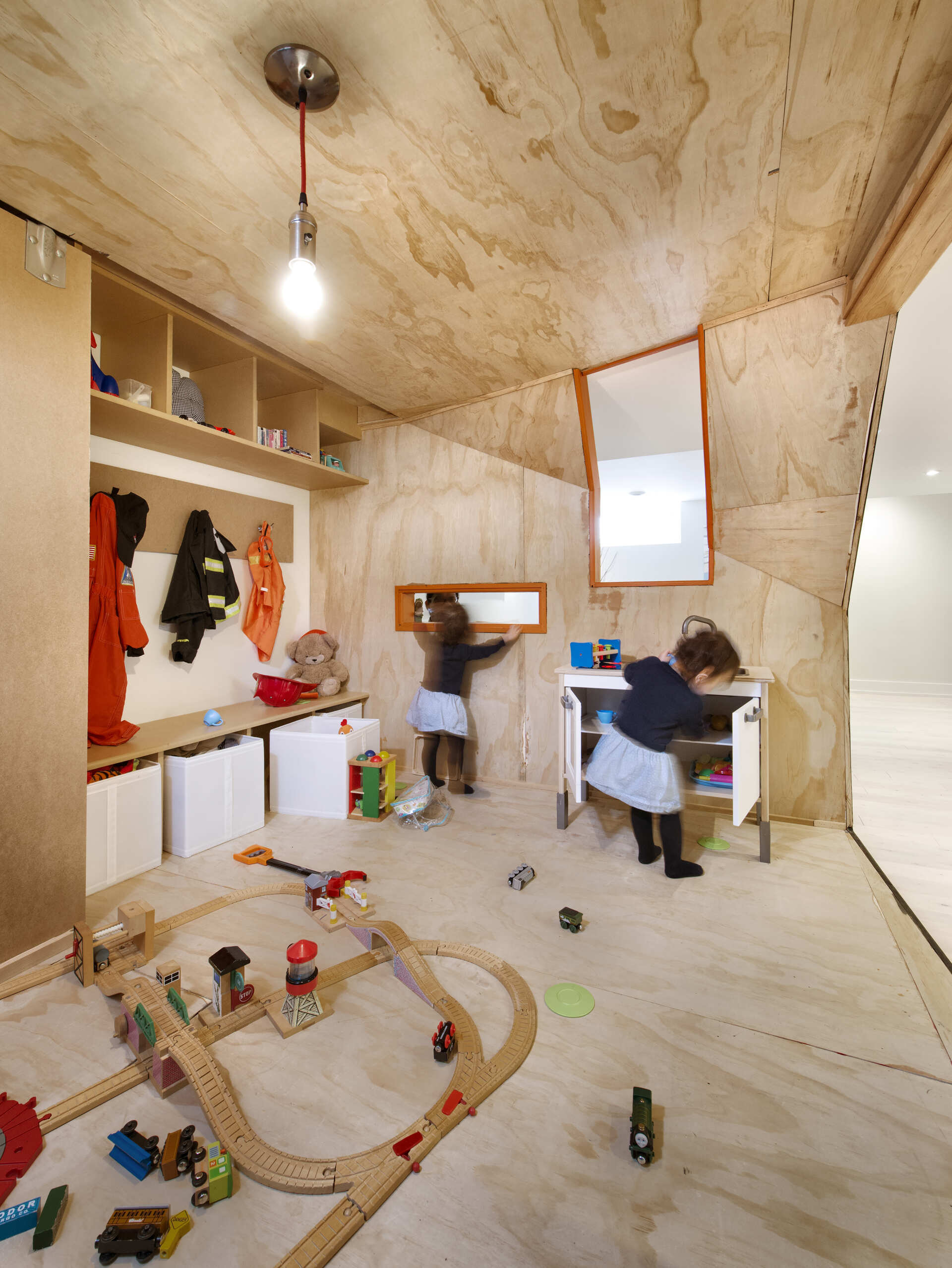 A creative children's playhouse built inside an Ottawa basement features dark reclaimed wood, bright orange windows, plywood interiors, and built-in toy storage. Designed by 25:8 Architecture + Urban Design, the miniature house creates a fun play area beside the family living room.
