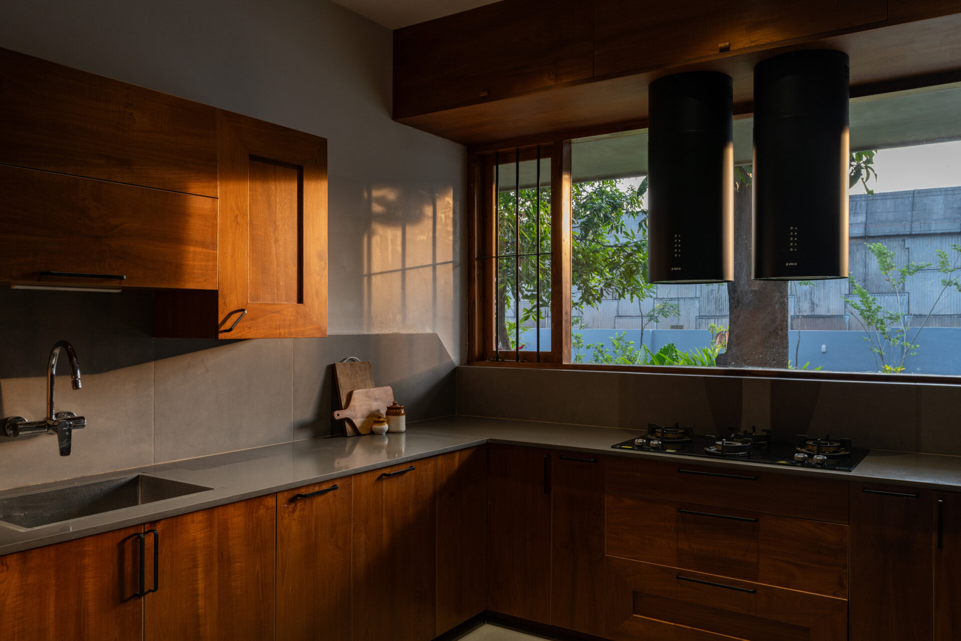 This contemporary U-shaped kitchen combines wood cabinets, quartz countertops, black range hoods, and a large garden-facing window that welcomes morning sunlight.