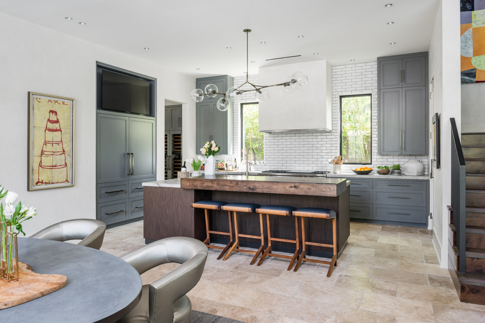A contemporary kitchen with gray cabinets, white subway tile, stone countertops, a dark wood island, rustic wood breakfast bar, and modern glass globe pendant lighting.