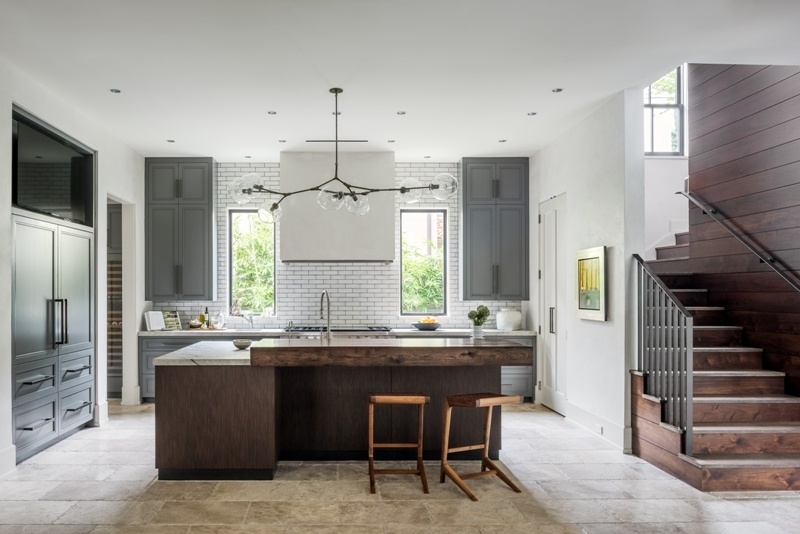 A contemporary kitchen with gray cabinets, white subway tile, stone countertops, a dark wood island, rustic wood breakfast bar, and modern glass globe pendant lighting.