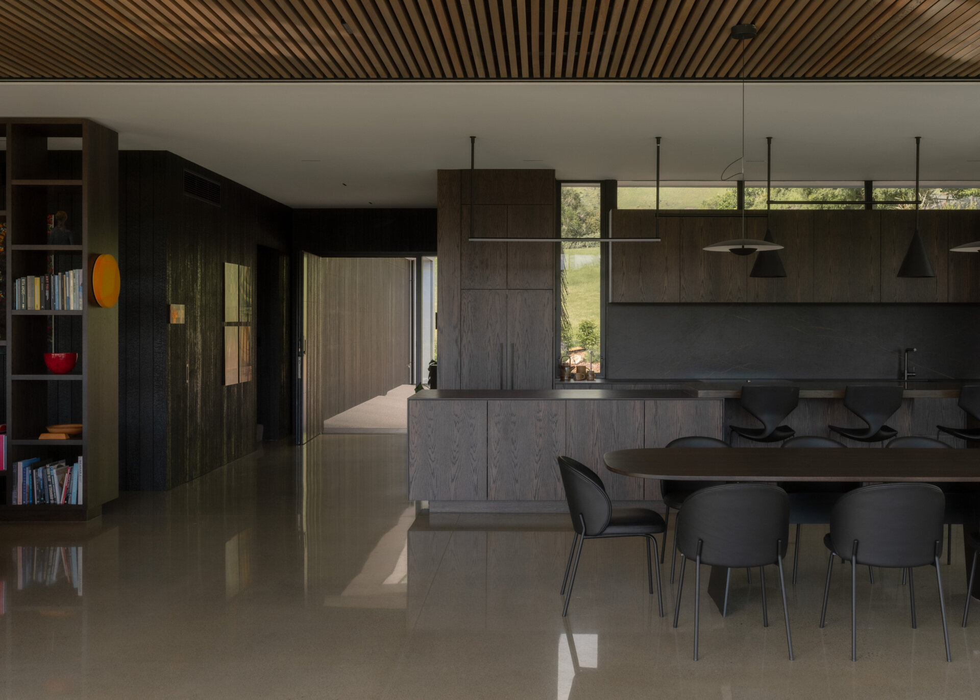 A contemporary dark oak kitchen with black marble countertops and backsplash, minimalist cabinetry, a long breakfast bar, black pendant lights, and polished concrete floors.