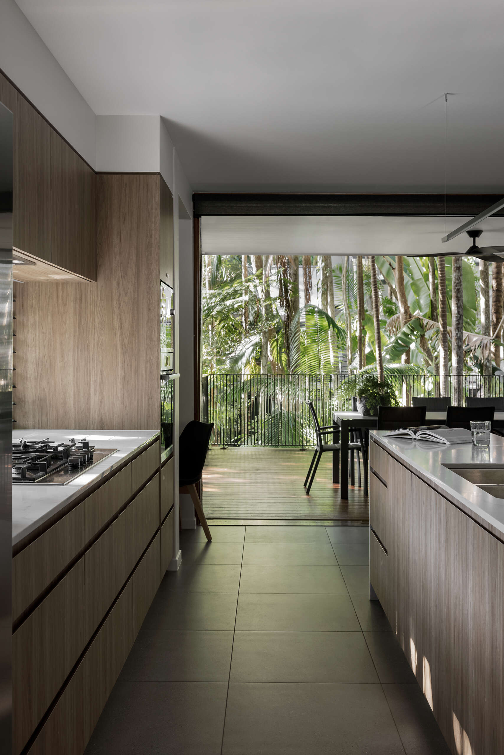Explore the modern kitchen at Raintree in Noosa Heads, Australia, featuring natural timber cabinetry, a white marble-look island, an extended timber breakfast bar, integrated appliances, and a curved plaster wall.