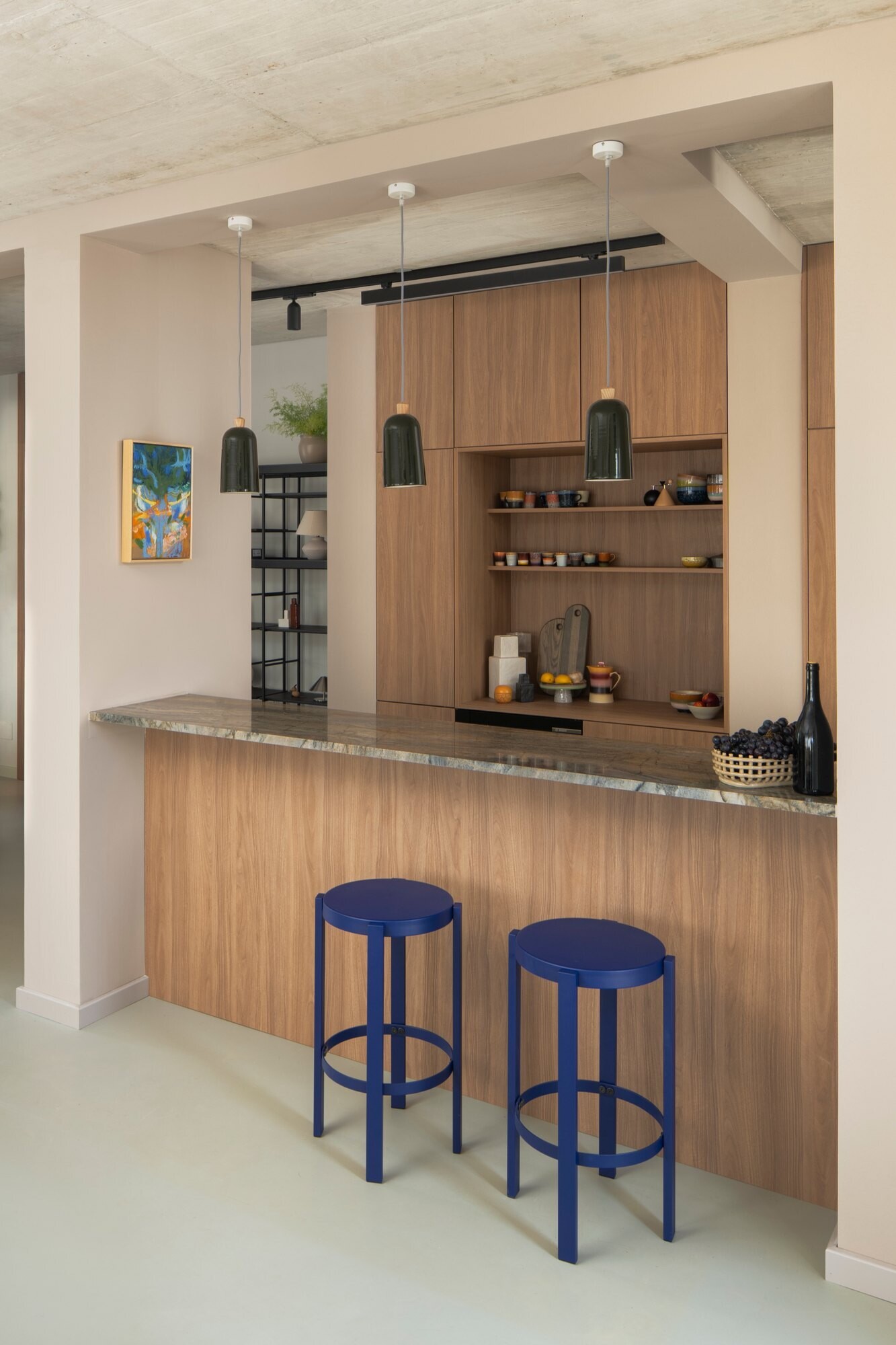 Get inspired by the kitchen at Arc House in Istria, featuring natural wood cabinetry, sage-green kitchen cabinets, a stone breakfast bar, cobalt-blue stools, open shelving and dark green pendant lights.