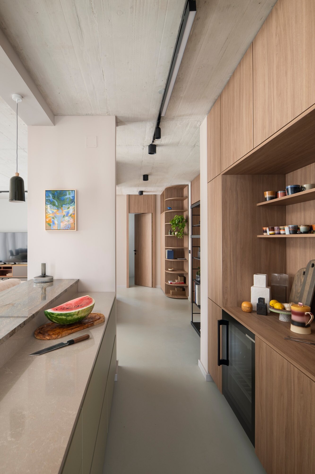 Get inspired by the kitchen at Arc House in Istria, featuring natural wood cabinetry, sage-green kitchen cabinets, a stone breakfast bar, cobalt-blue stools, open shelving and dark green pendant lights.