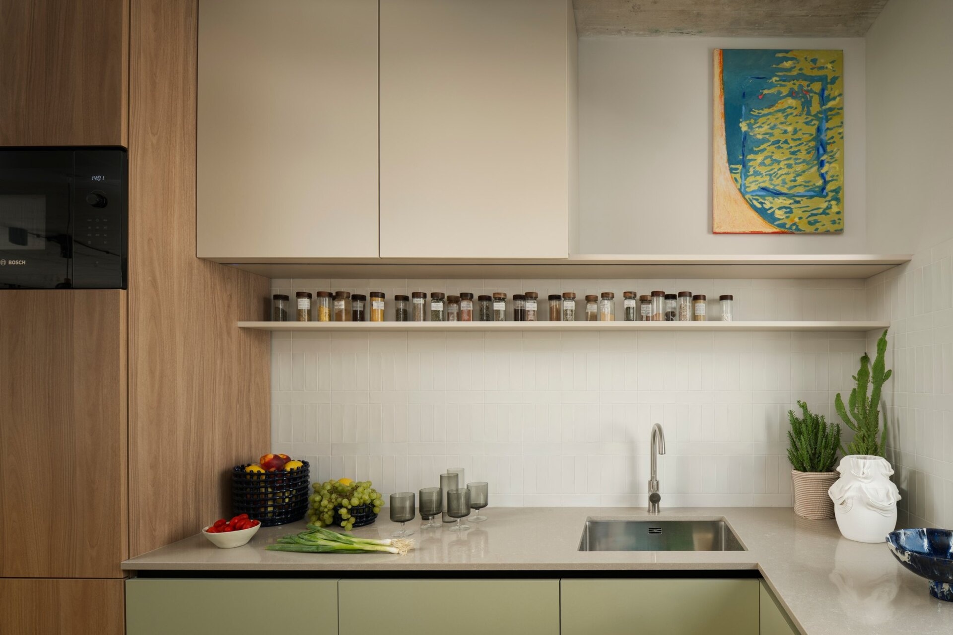 Get inspired by the kitchen at Arc House in Istria, featuring natural wood cabinetry, sage-green kitchen cabinets, a stone breakfast bar, cobalt-blue stools, open shelving and dark green pendant lights.