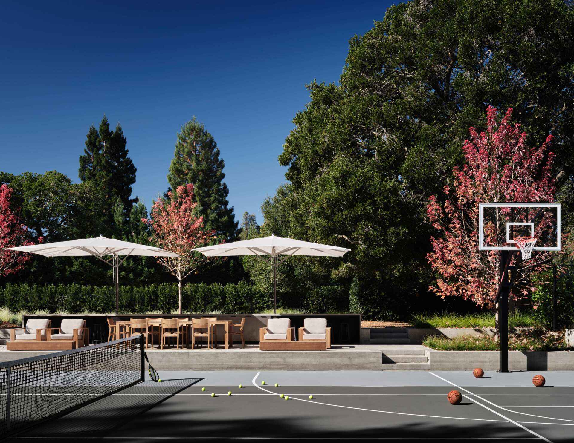 Explore the recreational facilities at this 3.5-acre California home, featuring a private tennis and basketball court, soccer field, and outdoor entertaining terrace. Timber furniture, white umbrellas, and landscaped gardens create a welcoming space for sports and social gatherings.