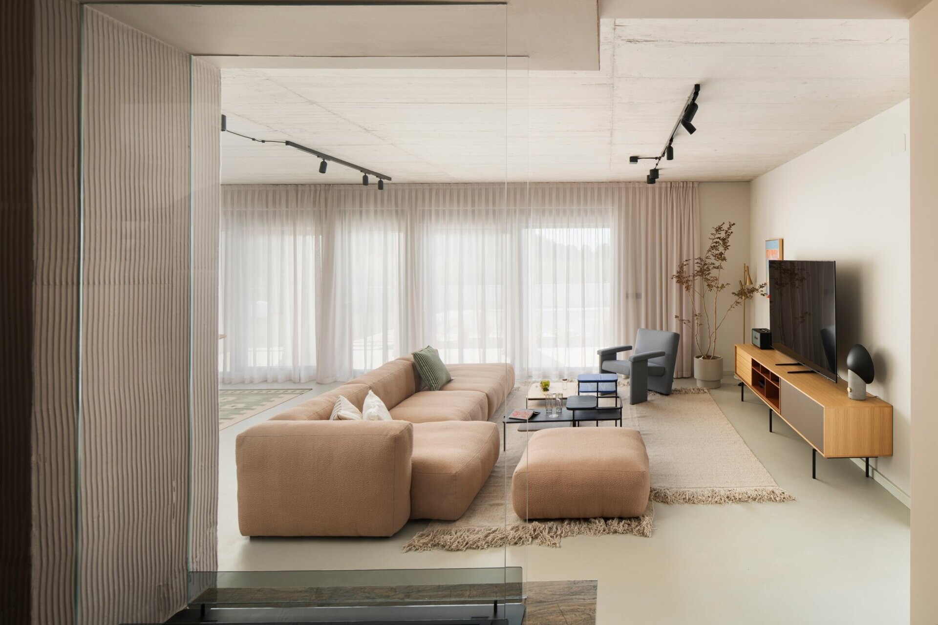 Explore the living room of Arc House in Istria, featuring a peach modular sofa, blue-grey lounge chair, modern coffee tables, exposed concrete ceiling, sheer curtains and warm contemporary interior styling by Jana Piacun.