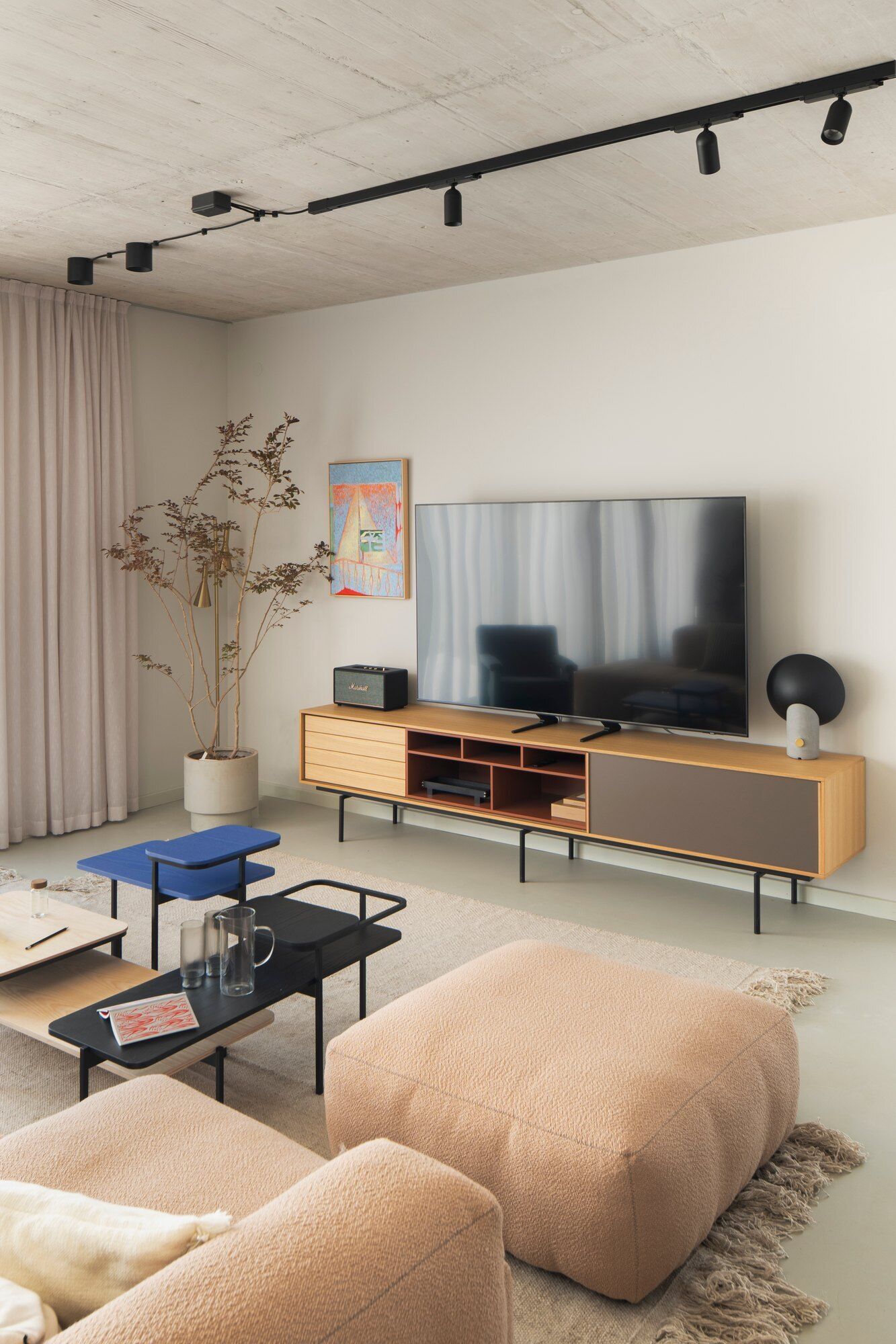Explore the living room of Arc House in Istria, featuring a peach modular sofa, blue-grey lounge chair, modern coffee tables, exposed concrete ceiling, sheer curtains and warm contemporary interior styling by Jana Piacun.