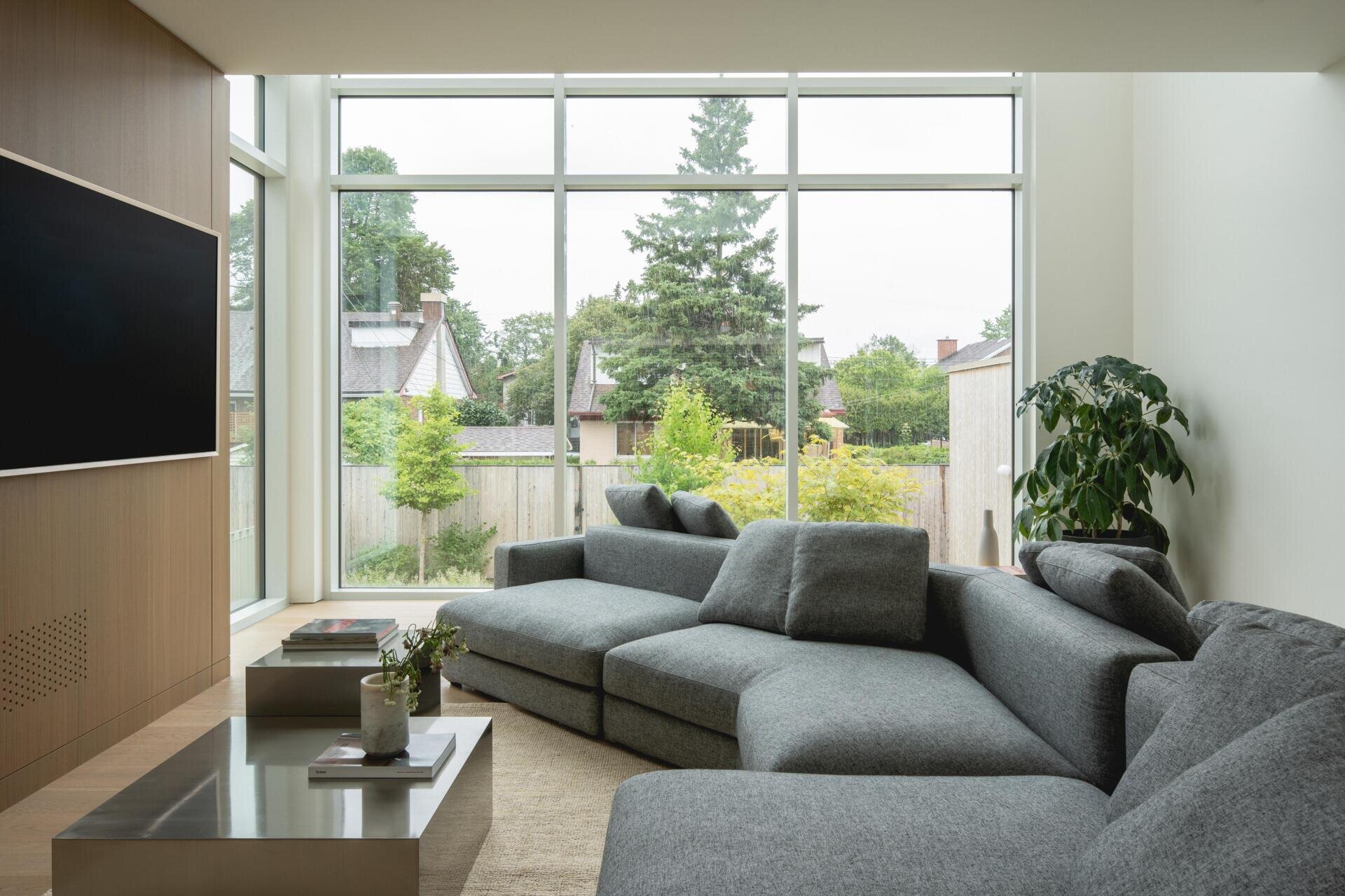 Step inside the double-height living room of The Lens in Montreal. Designed by MU Architecture, the minimalist space features a large grey sectional sofa, pale wood panelling, and floor-to-ceiling windows overlooking the garden.