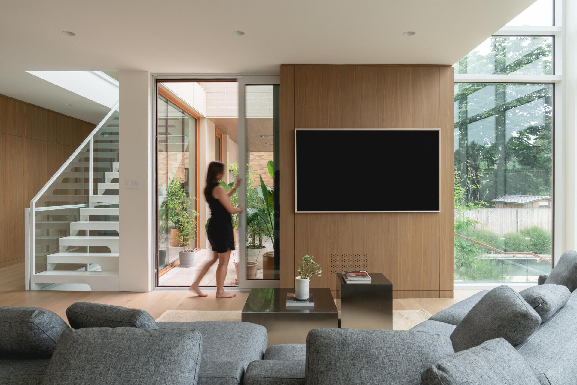 Step inside the double-height living room of The Lens in Montreal. Designed by MU Architecture, the minimalist space features a large grey sectional sofa, pale wood panelling, and floor-to-ceiling windows overlooking the garden.