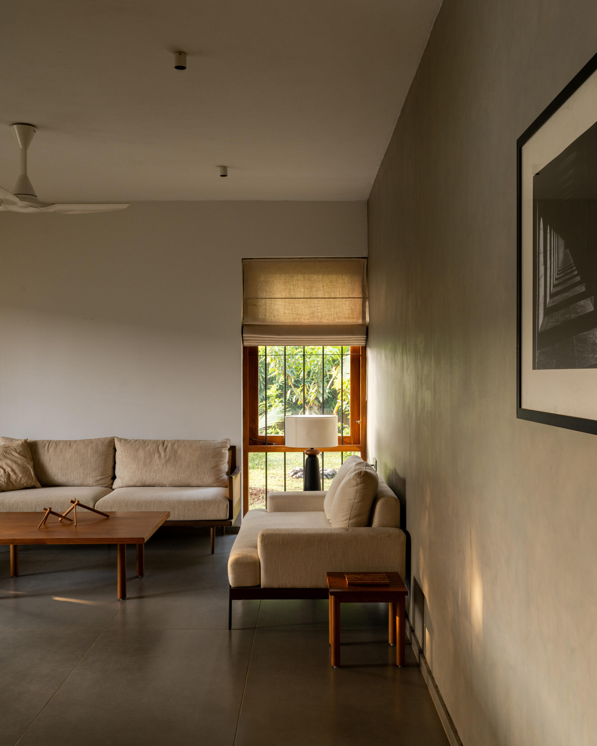 Discover a contemporary living room with large teak-framed windows, neutral furniture, wooden accents, and views of a lush tropical garden.