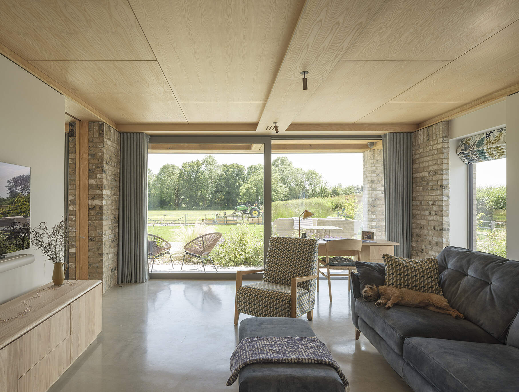 Exposed brick columns, pale wood ceilings, large sliding glass doors, and polished concrete floors bring natural textures into this contemporary open-plan home.