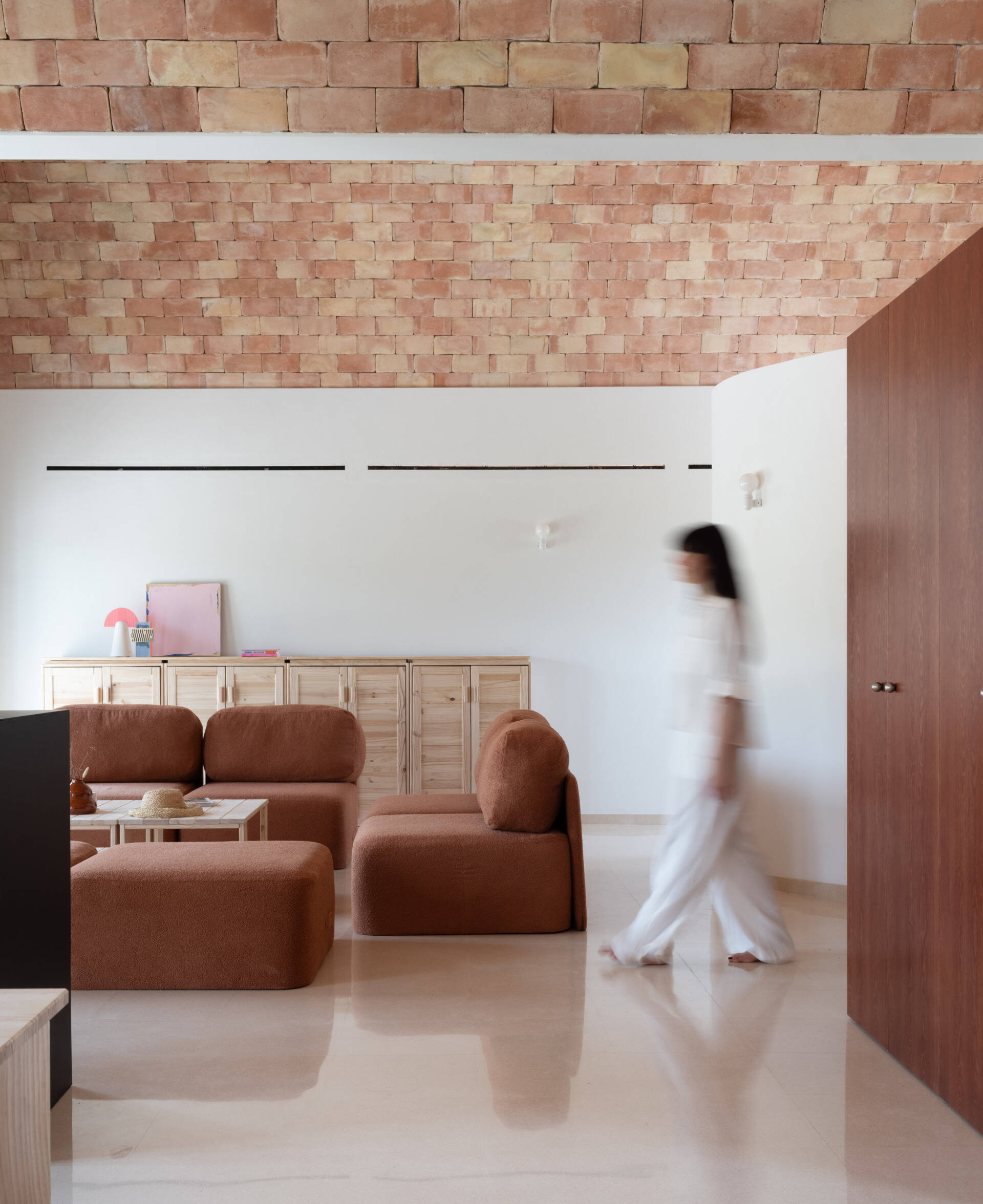 Step inside the living room of Casa Vereda in Spain, where a dramatic curved brick ceiling rises above rust-coloured modular sofas, terrazzo flooring, and contemporary timber furniture. A beautiful combination of traditional Catalan architecture and modern interior design.