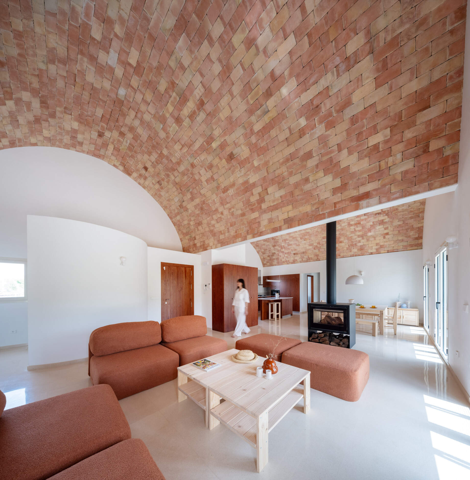 Step inside the living room of Casa Vereda in Spain, where a dramatic curved brick ceiling rises above rust-coloured modular sofas, terrazzo flooring, and contemporary timber furniture. A beautiful combination of traditional Catalan architecture and modern interior design.