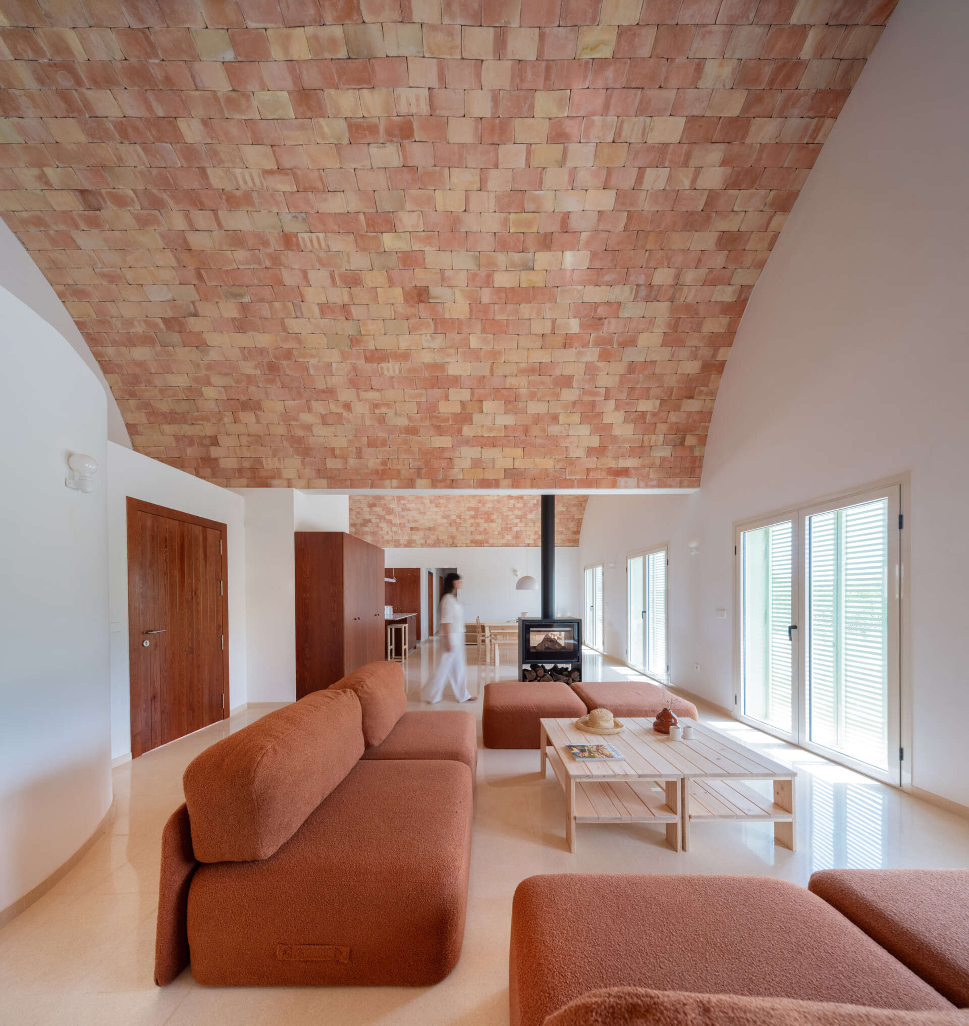 Step inside the living room of Casa Vereda in Spain, where a dramatic curved brick ceiling rises above rust-coloured modular sofas, terrazzo flooring, and contemporary timber furniture. A beautiful combination of traditional Catalan architecture and modern interior design.