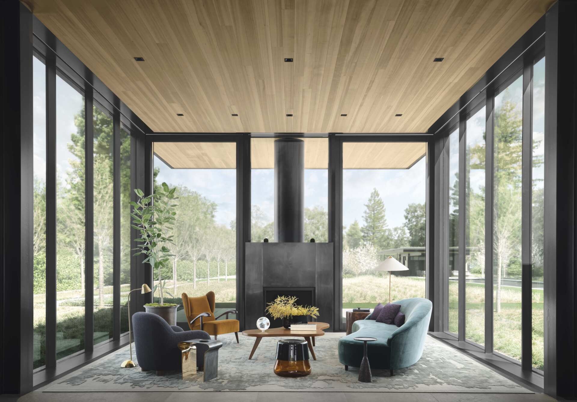  A curved blue-green sofa, rounded lounge chairs, sculptural furniture, and a contemporary black fireplace create a colorful interior surrounded by garden views at this California home.