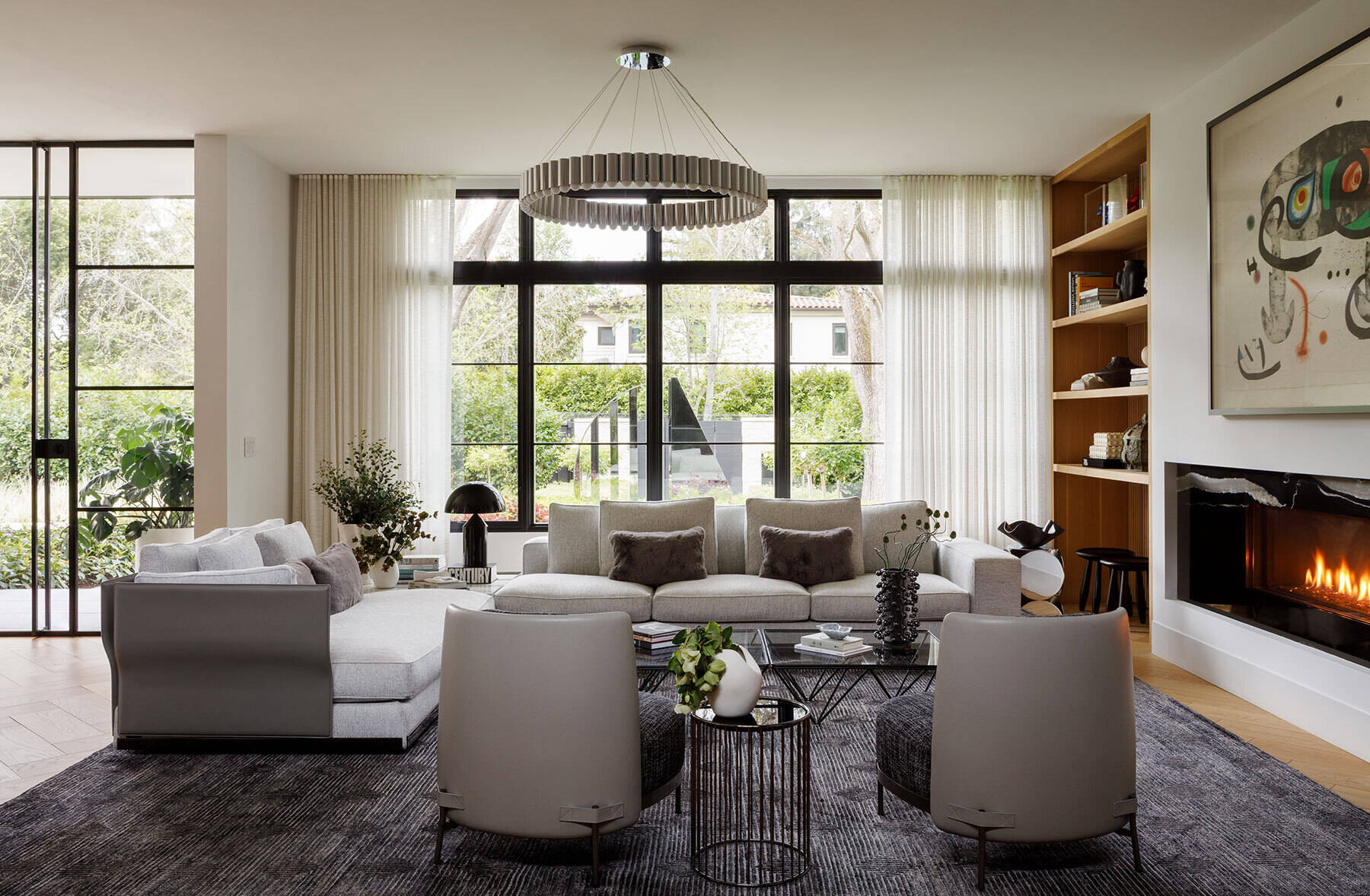 Inside the Atherton Residence living room by Paulina Carcach Studio, a Minotti sectional, Lee Broom Carousel chandelier, bleached-oak shelving, fireplace and curated collection of art and objects create a warm modern interior.