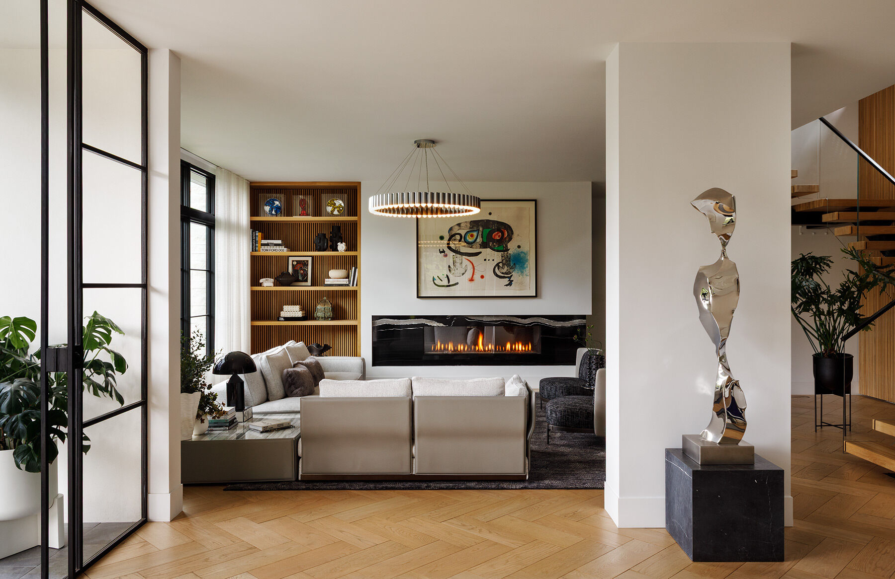 Inside the Atherton Residence living room by Paulina Carcach Studio, a Minotti sectional, Lee Broom Carousel chandelier, bleached-oak shelving, fireplace and curated collection of art and objects create a warm modern interior.