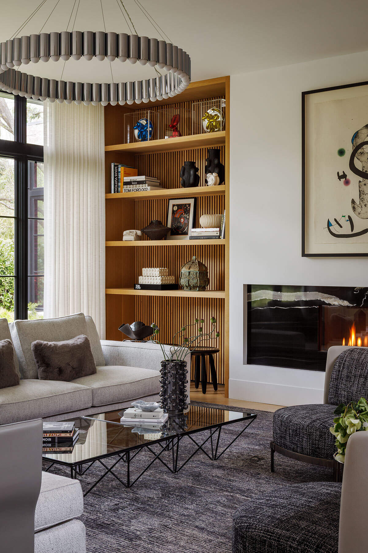 Inside the Atherton Residence living room by Paulina Carcach Studio, a Minotti sectional, Lee Broom Carousel chandelier, bleached-oak shelving, fireplace and curated collection of art and objects create a warm modern interior.
