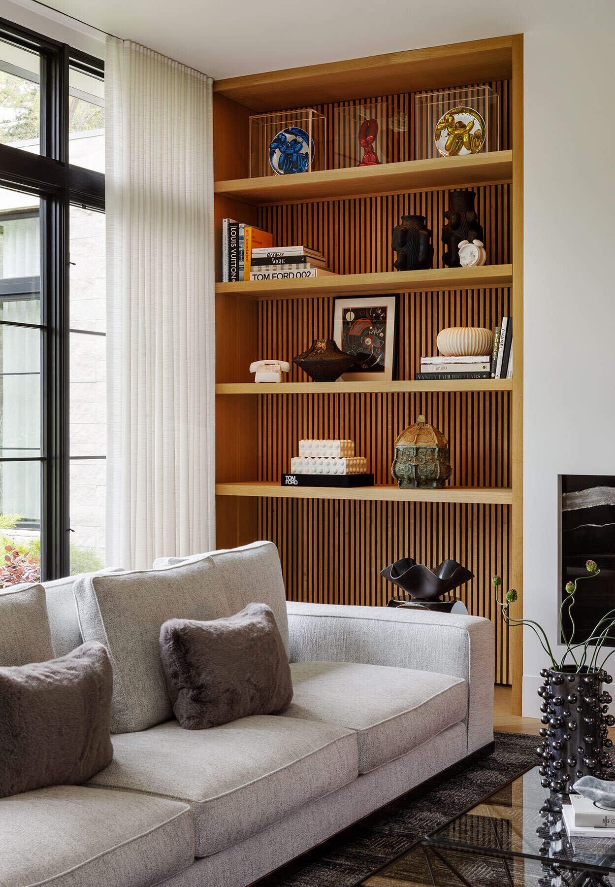 Inside the Atherton Residence living room by Paulina Carcach Studio, a Minotti sectional, Lee Broom Carousel chandelier, bleached-oak shelving, fireplace and curated collection of art and objects create a warm modern interior.
