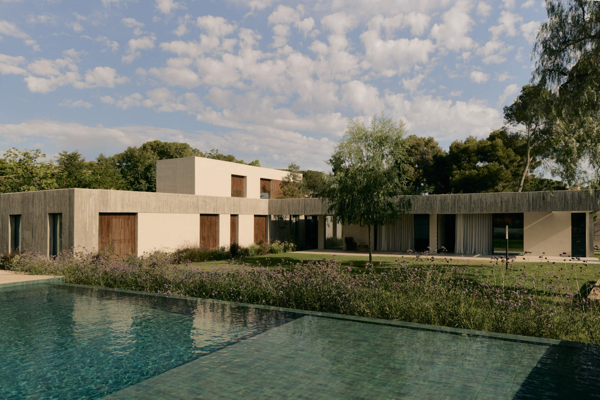 Explore a modern Spanish home's landscaped backyard with an elevated swimming pool, flowering gardens, a shaded concrete patio, and contemporary outdoor furniture.