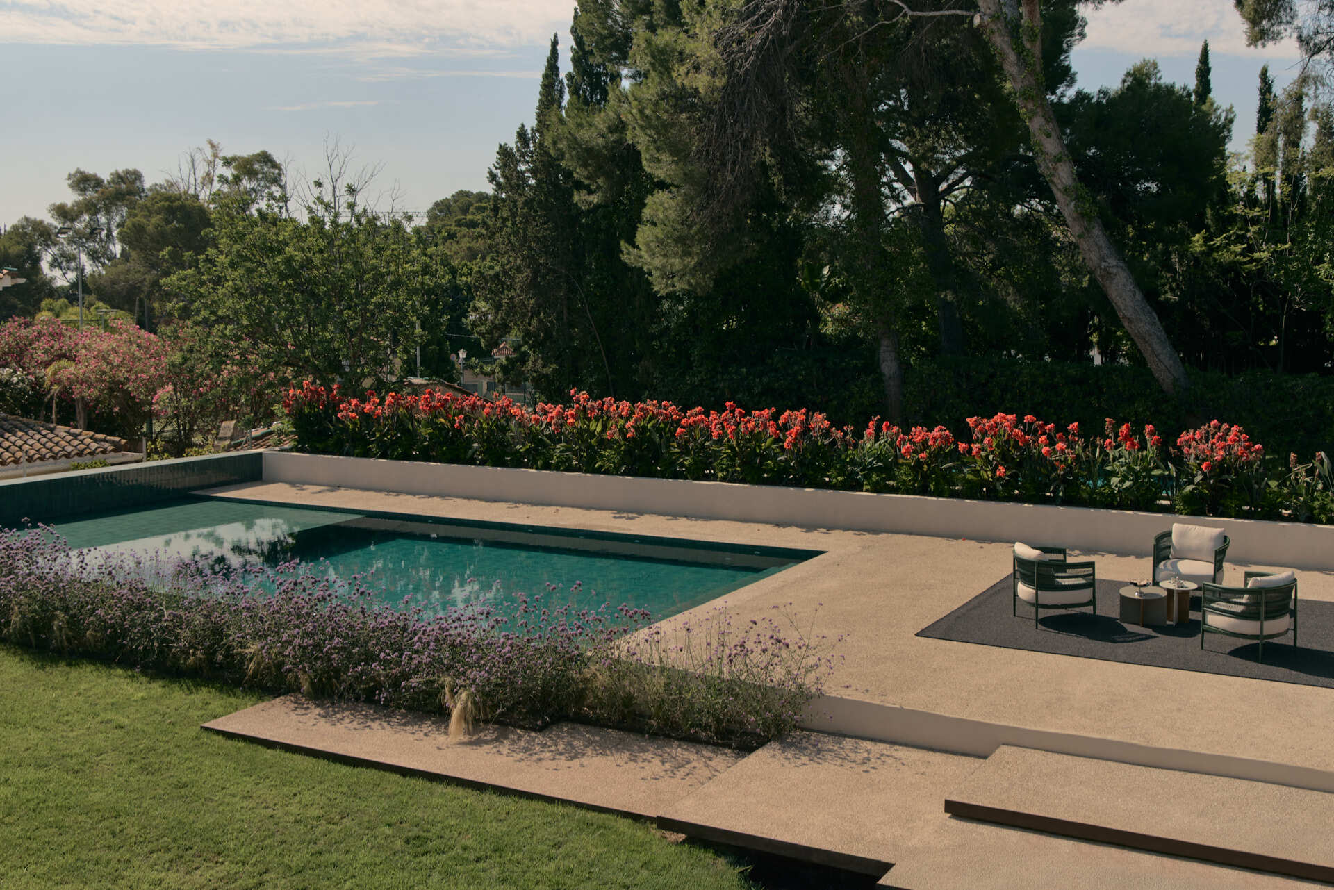 Explore a modern Spanish home's landscaped backyard with an elevated swimming pool, flowering gardens, a shaded concrete patio, and contemporary outdoor furniture.