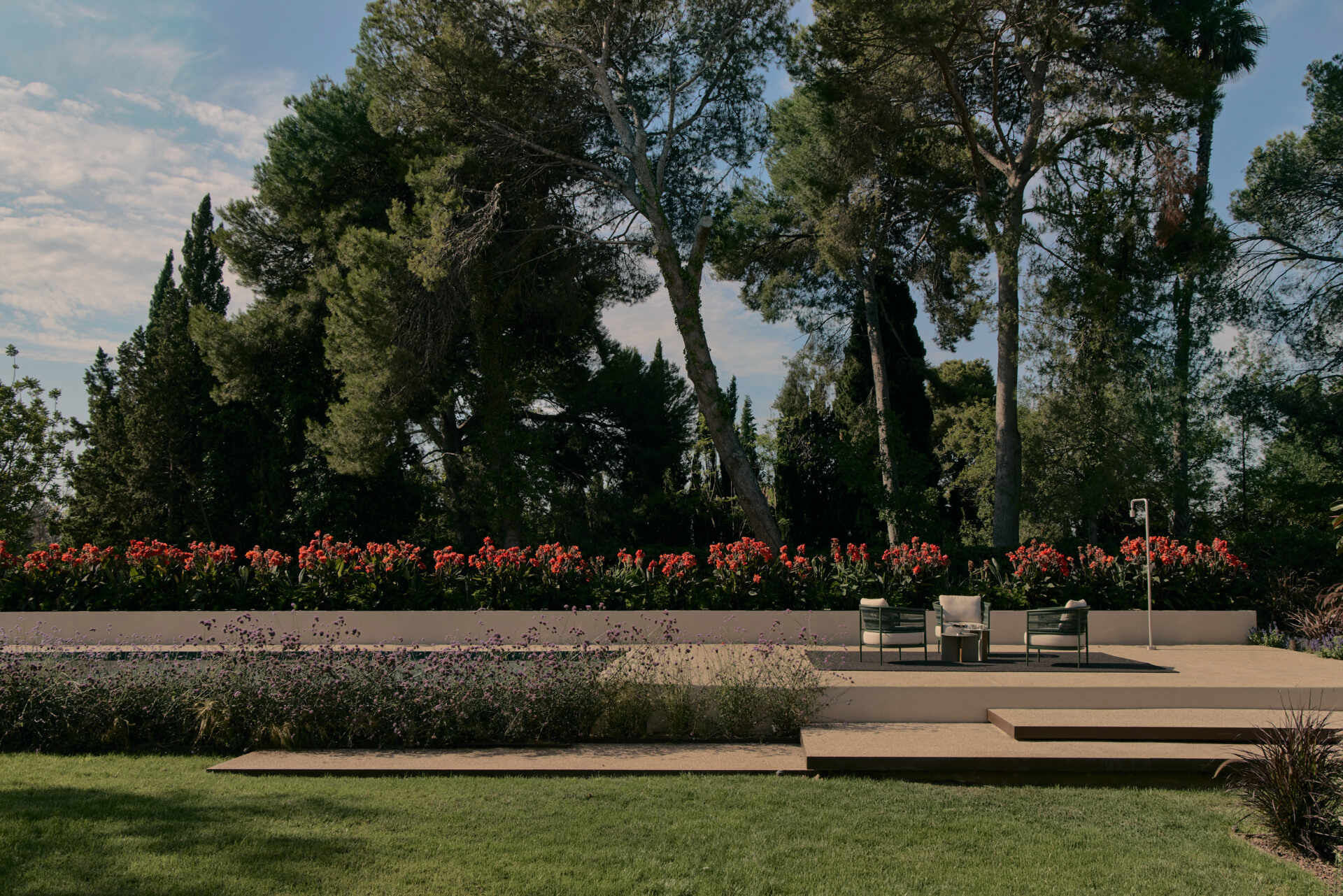 Explore a modern Spanish home's landscaped backyard with an elevated swimming pool, flowering gardens, a shaded concrete patio, and contemporary outdoor furniture.