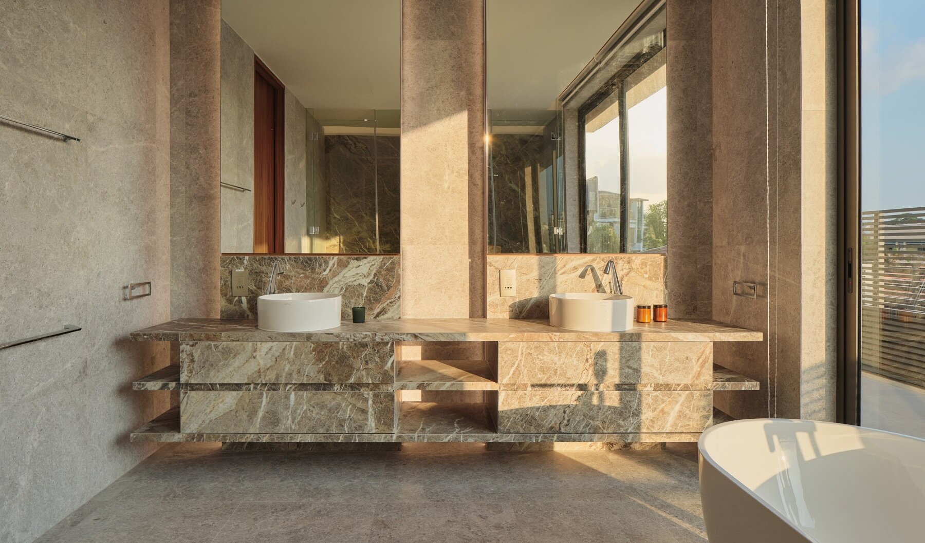 Explore the primary bathroom of this Singapore home, featuring a floating marble double vanity, vessel sinks, a freestanding bathtub, glass shower enclosures, and natural stone finishes.