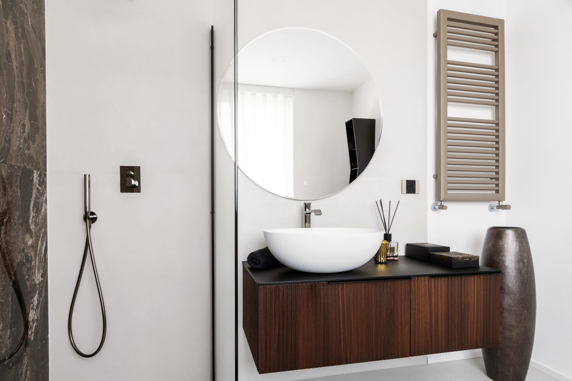 A modern primary bathroom features dramatic marble-look shower tiles, a frameless glass enclosure, a floating dark timber vanity, and a large round mirror.