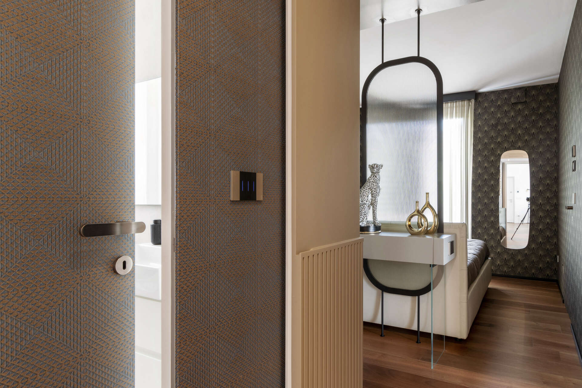 A hidden guest bathroom features dramatic tree-pattern wallpaper, a floating vanity, a large mirror, and a dark tiled shower, accessed from a textured hallway.