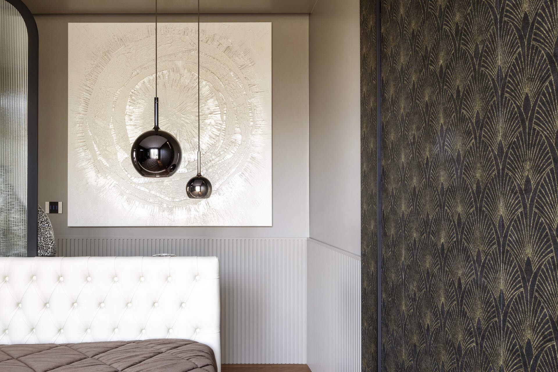 This primary bedroom features Art Deco wallpaper, a white upholstered headboard, black pendant lights, and a custom dressing counter with an arched glass partition.