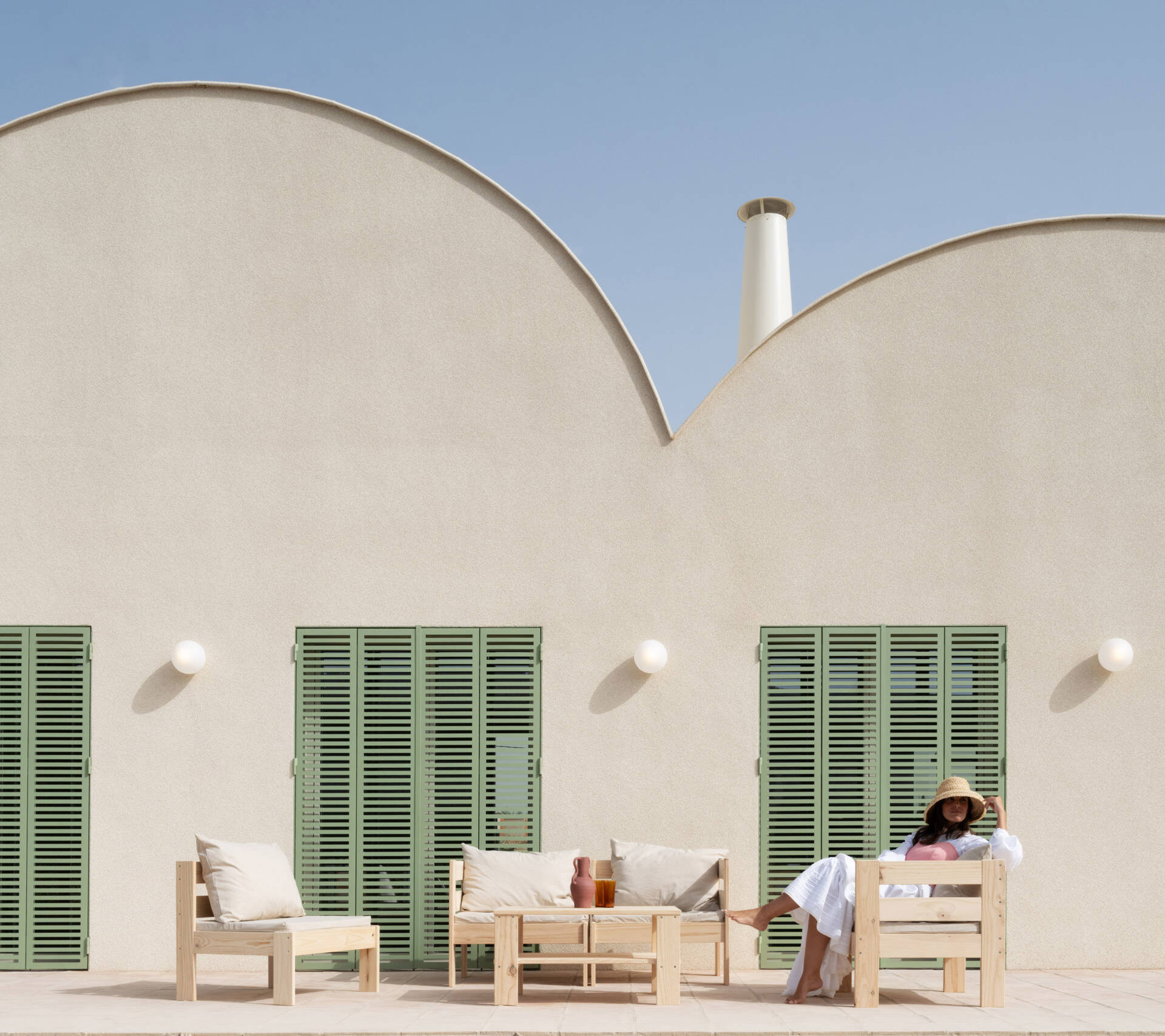 Explore the Mediterranean-inspired patio at Casa Vereda in Spain, featuring handcrafted terracotta flooring, pale timber outdoor furniture, sage-green shutters, and curved architecture. A beautiful example of contemporary outdoor living.