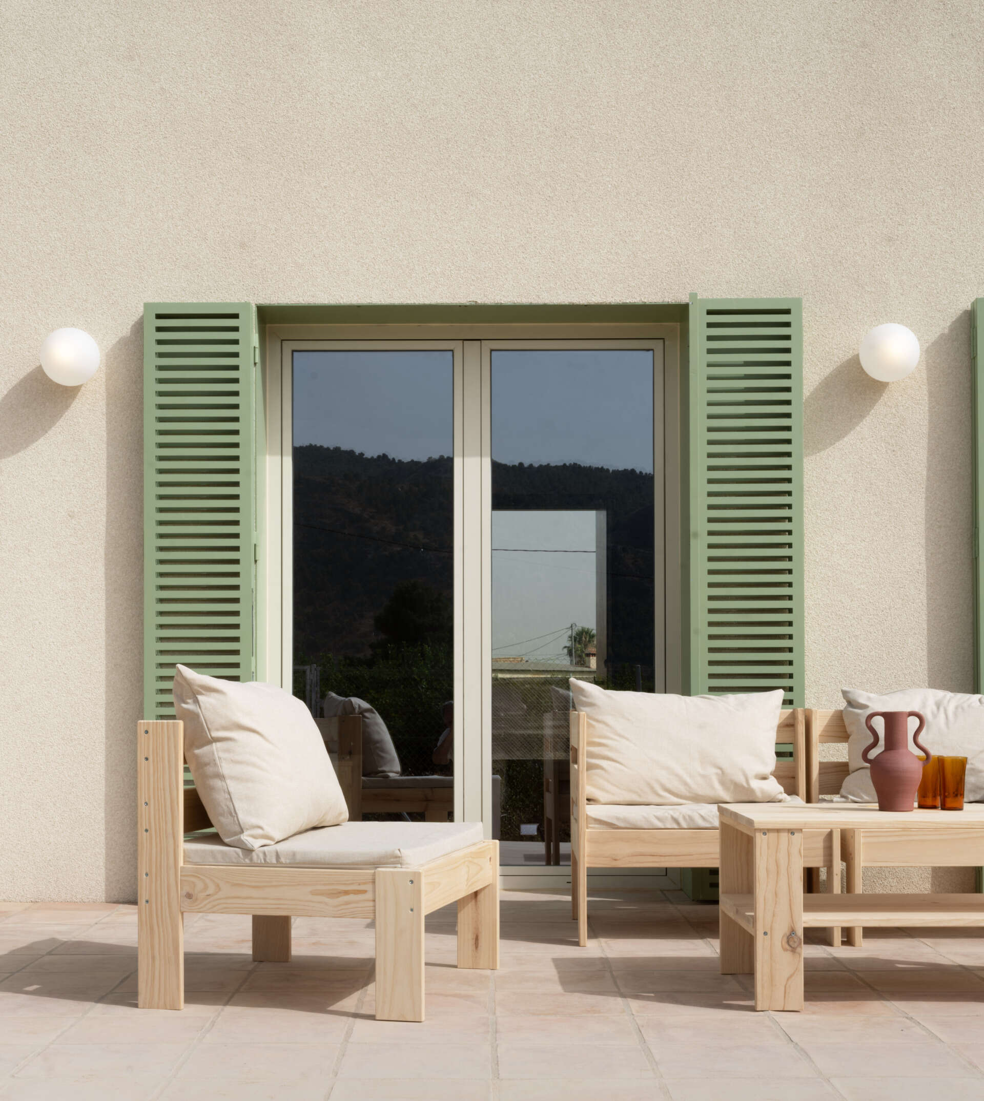 Explore the Mediterranean-inspired patio at Casa Vereda in Spain, featuring handcrafted terracotta flooring, pale timber outdoor furniture, sage-green shutters, and curved architecture. A beautiful example of contemporary outdoor living.