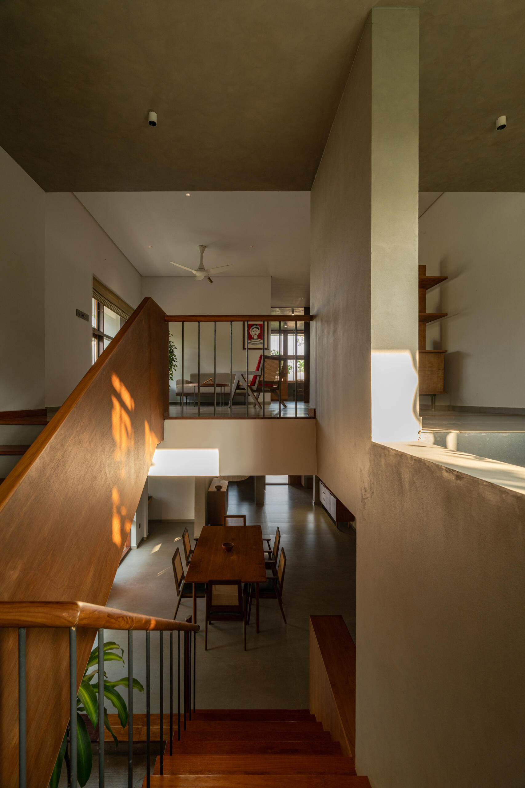 A timber staircase with a solid wooden balustrade and black metal railings links the floors of this contemporary Indian house, overlooking the dining space below.